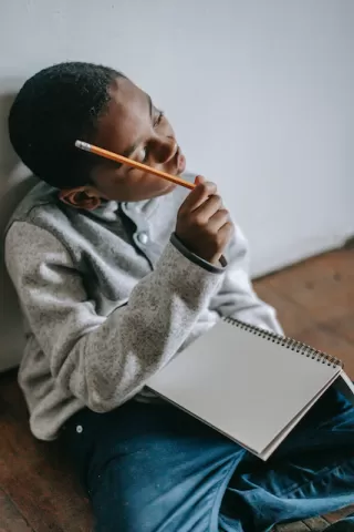 Boy pondering with a pencil and blank notebook.