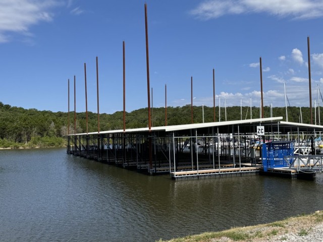 A peaceful marina with numerous empty boat slips extends into the calm water under a clear blue sky, surrounded by lush green hills, capturing a serene and inviting lakeside scene.