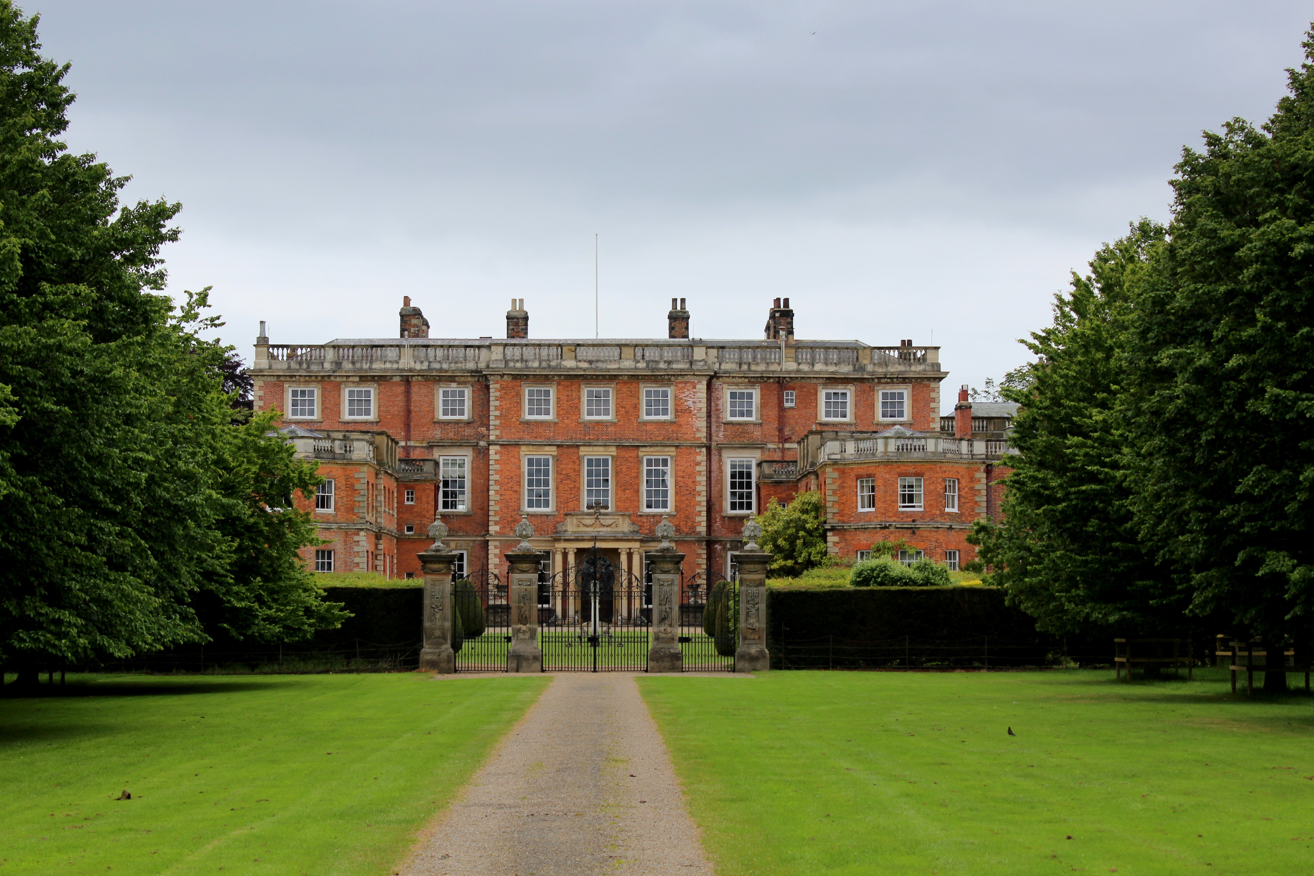 Historic English manor house with formal landscaped gardens featuring colorful flower borders and manicured lawn approach