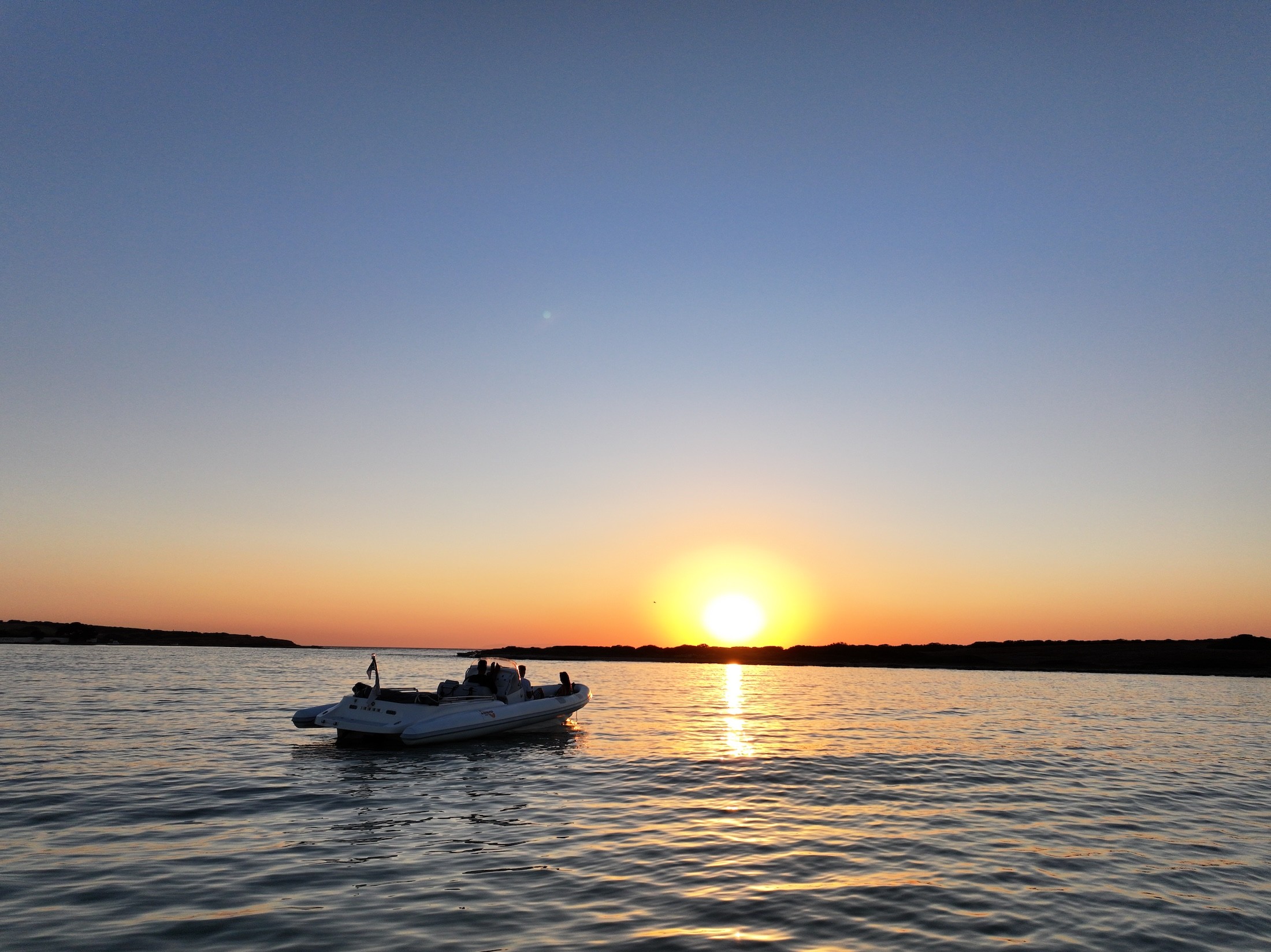 White Rock 36 speedboat with captain at helm cruising calm blue waters near Paros coastline with hills in background.