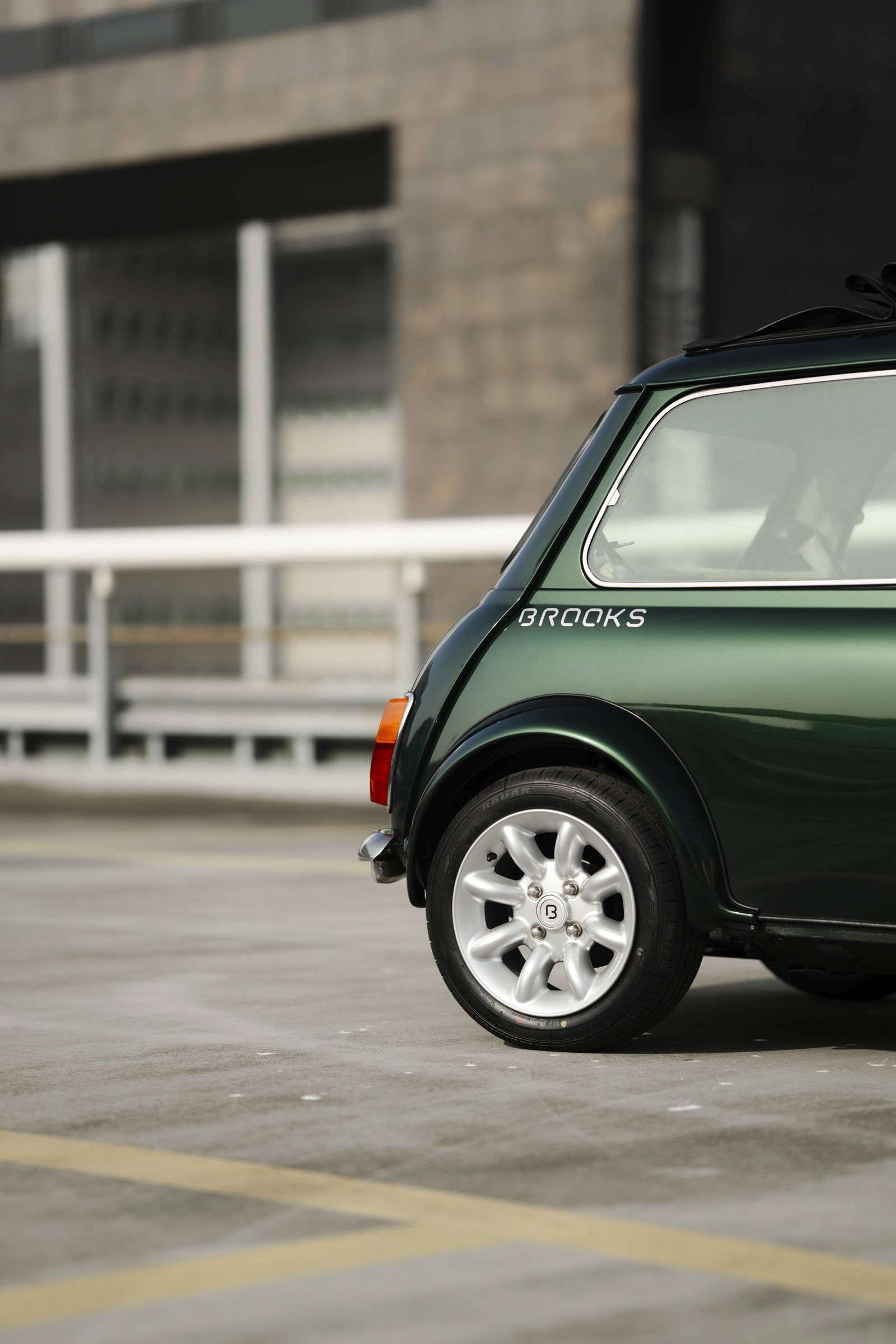 Close-up of a green car in a parking lot, focused on the rear wheel and angled toward a building.