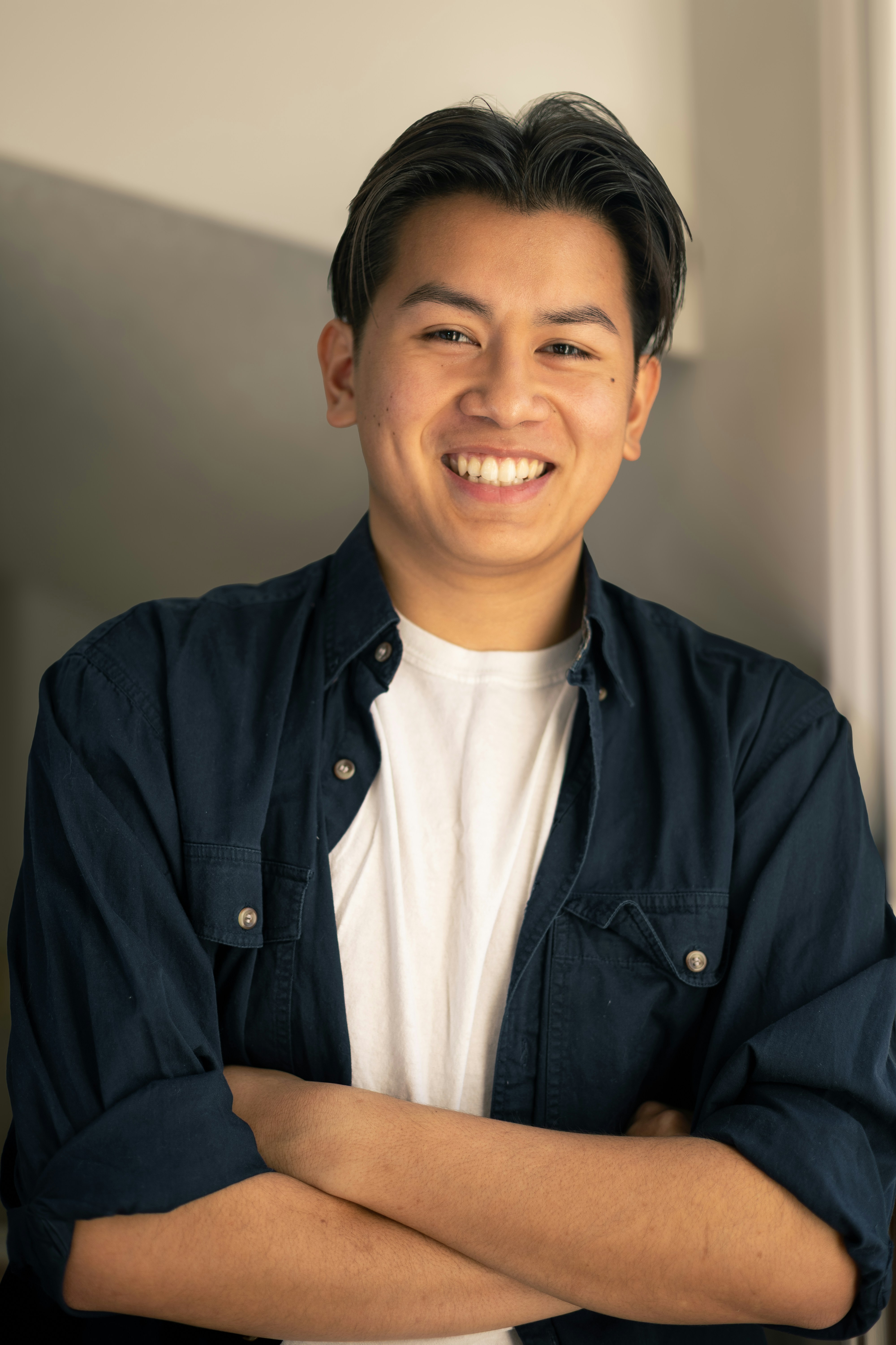 Young man in a blue shirt smiles with arms crossed.