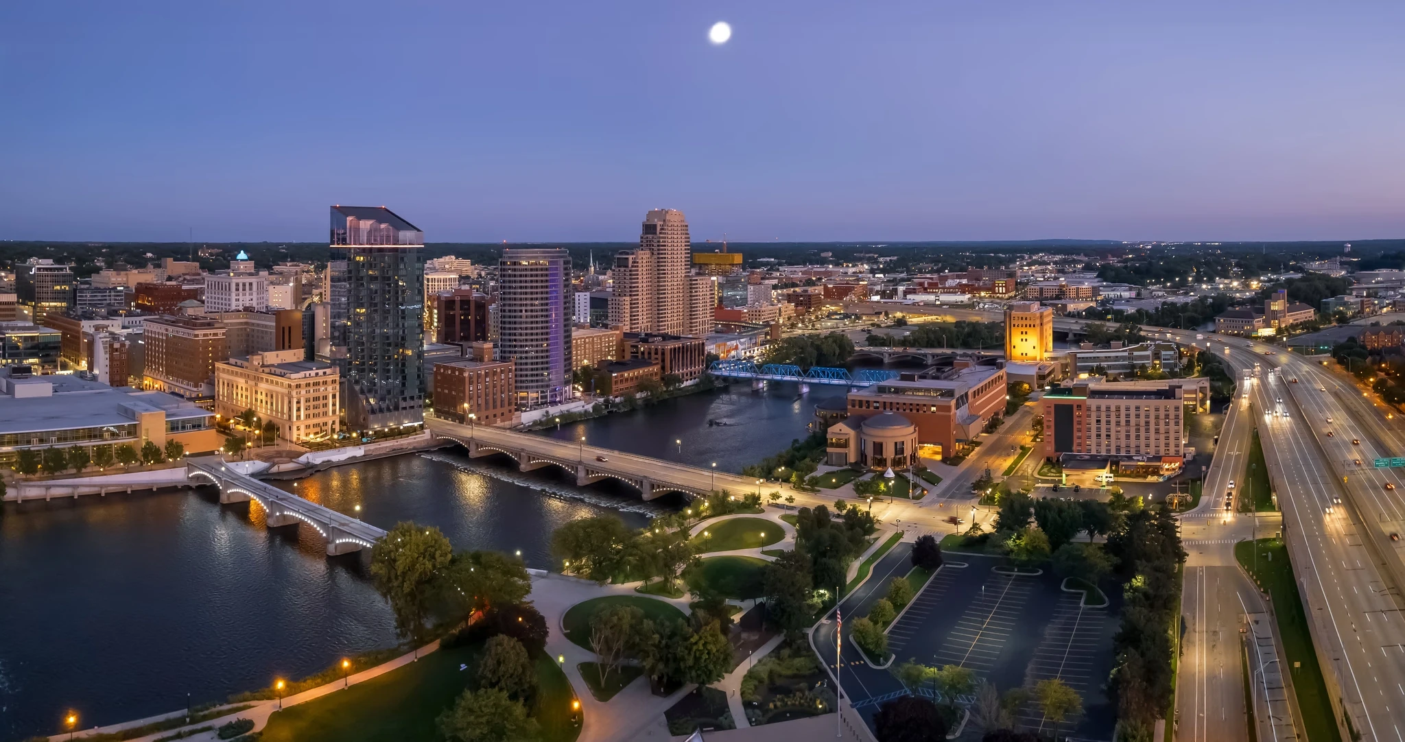 City skyline at dusk with a glowing moon in the background, casting a serene light over the urban landscape.