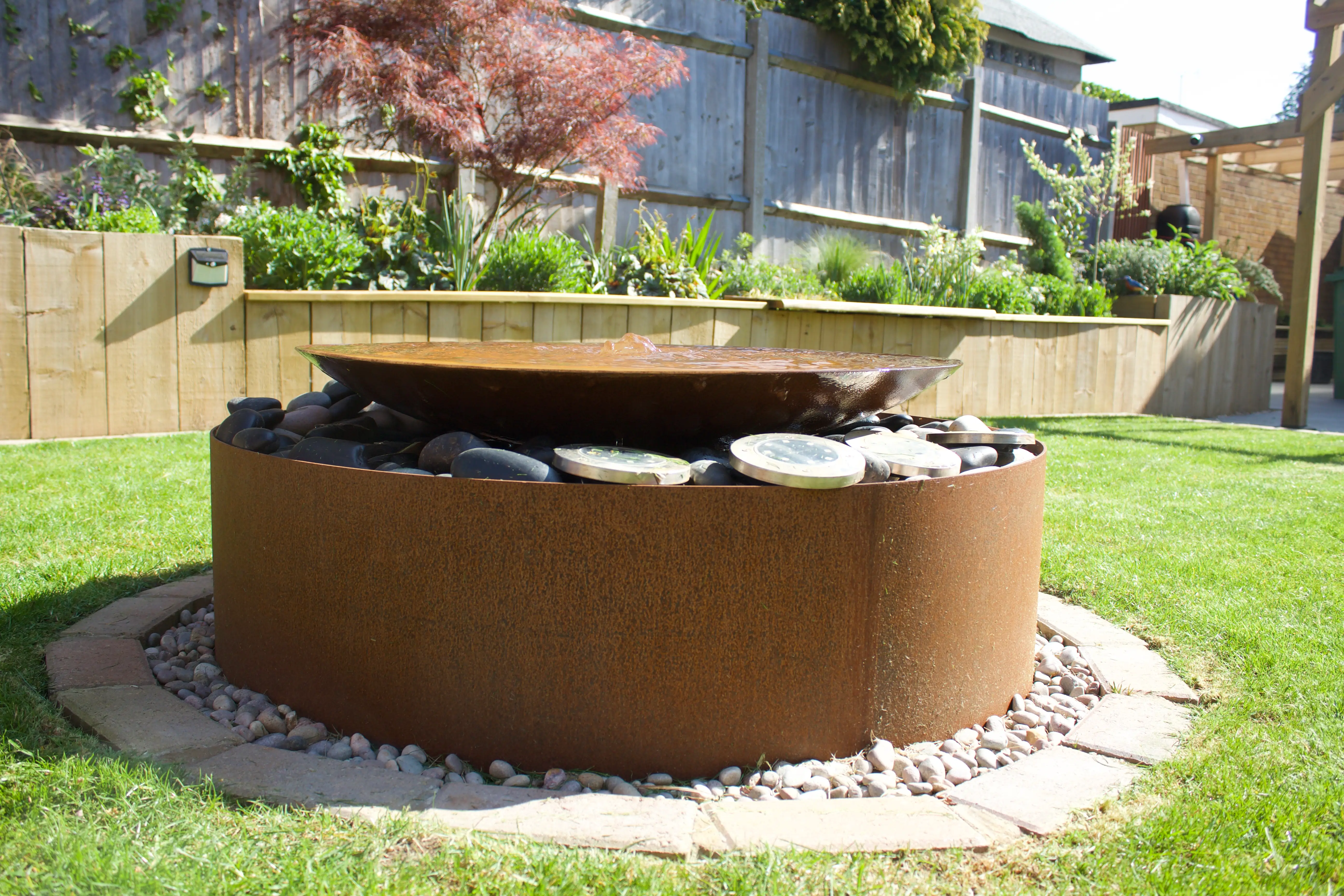 A circular fire pit surrounded by rocks, set on a grassy lawn with some greenery in the background.