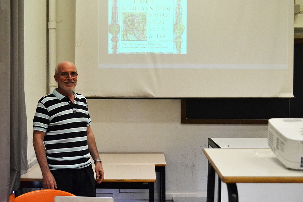an older man sitting on a class with an image projected on the wall behind him