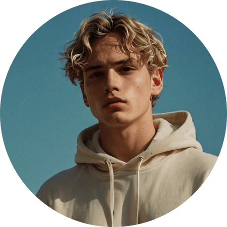 A young man with curly hair, wearing a hoodie, against a clear blue sky.
