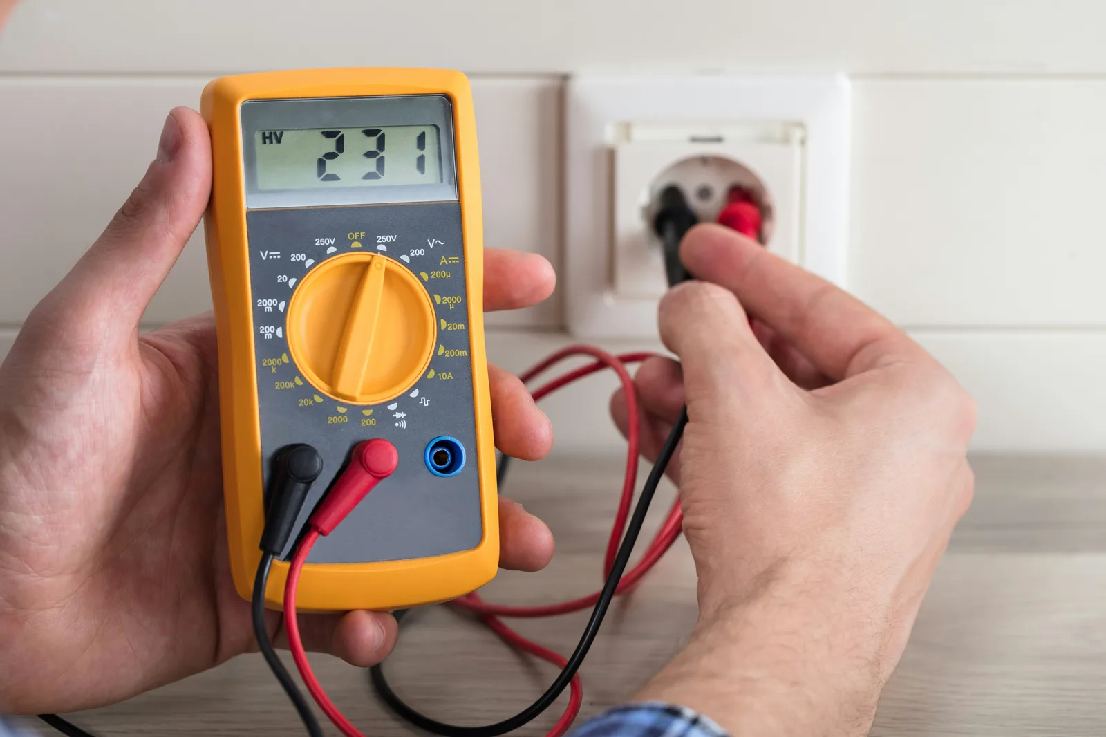Electrician using digital multimeter to measure voltage at outlet