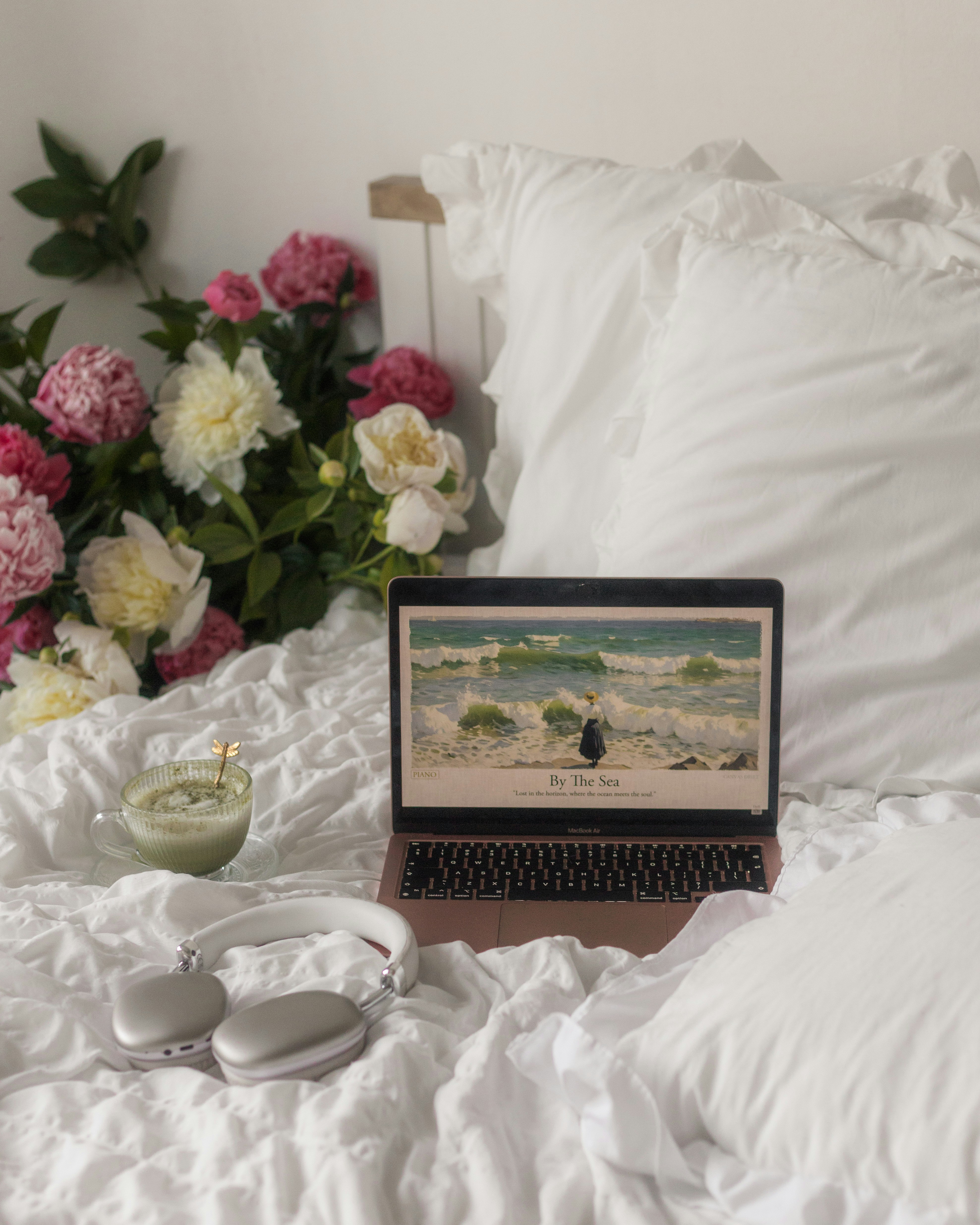 Laptop, headphones, and matcha on a bed with flowers.
