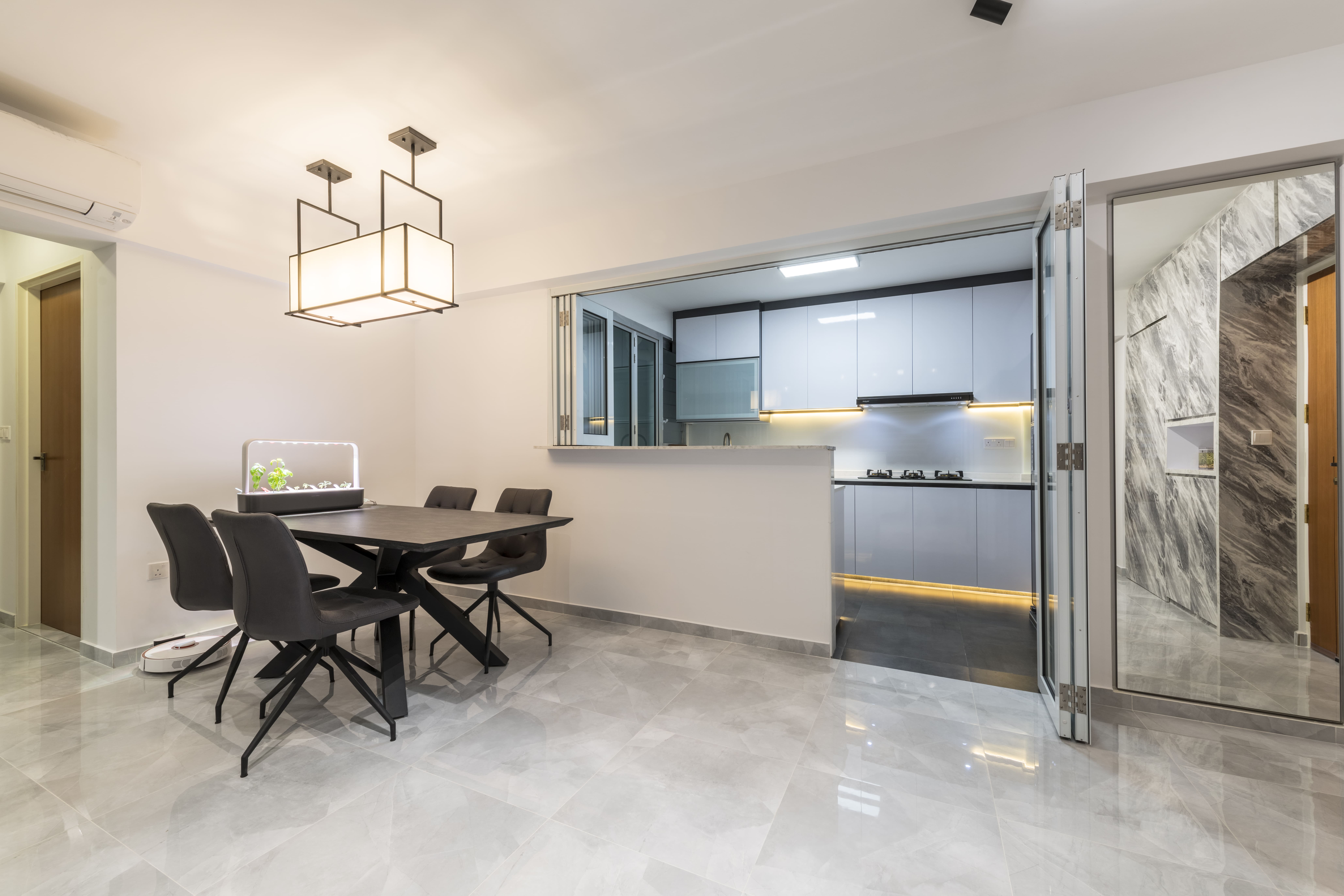The dining area connects to the open kitchen through a service hatch, showcasing a black dining table, matching chairs, and modern pendant lighting that anchors the space.