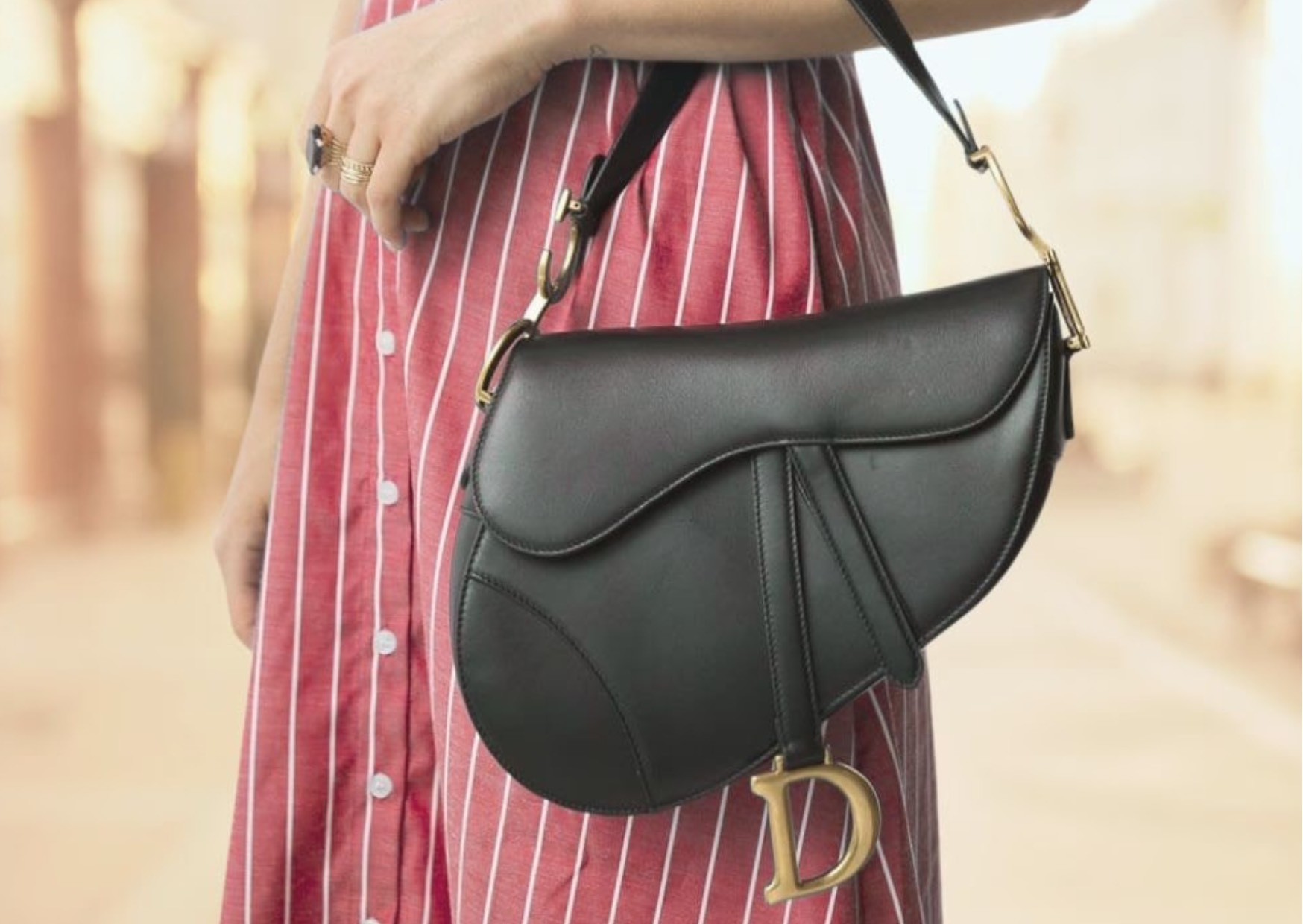 Fashionable woman wearing an elegant, chic, luxurious designer branded black leather Dior saddle bag with gold features, outdoors on the street. 