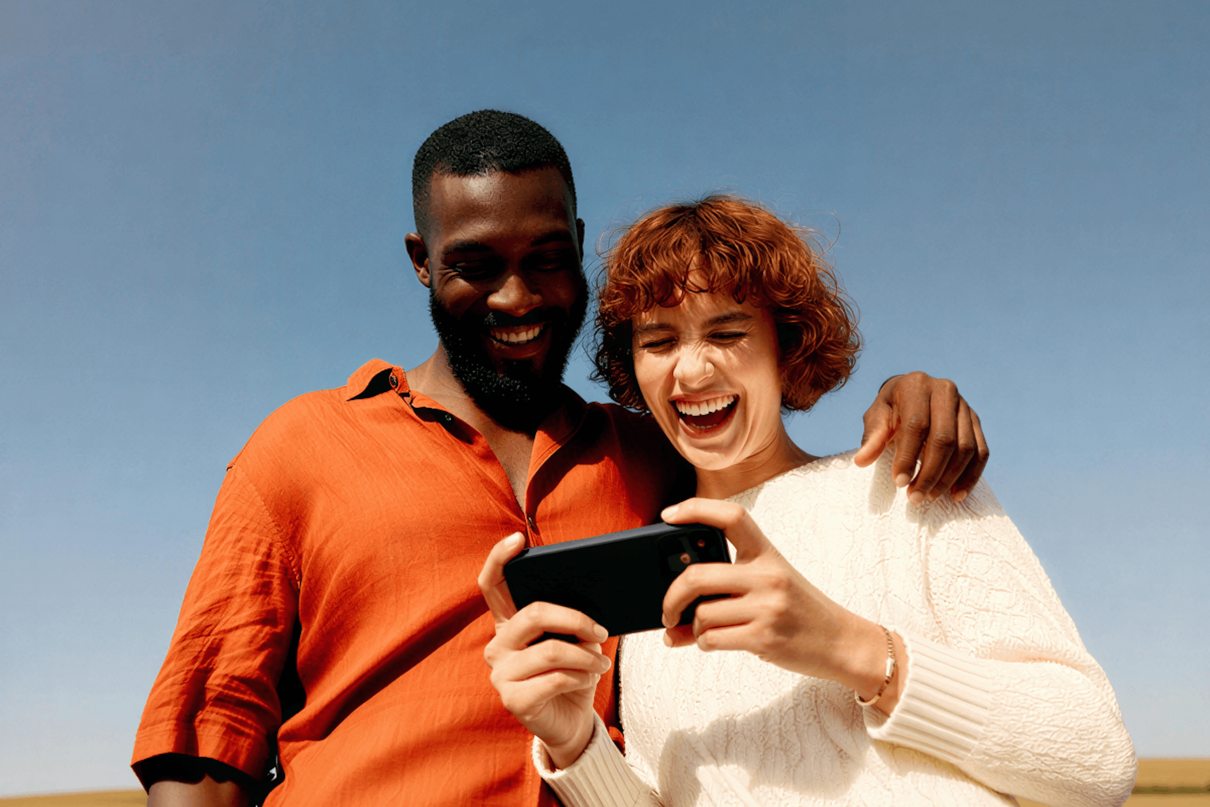 Two people smiling and standing close together against a simple background
