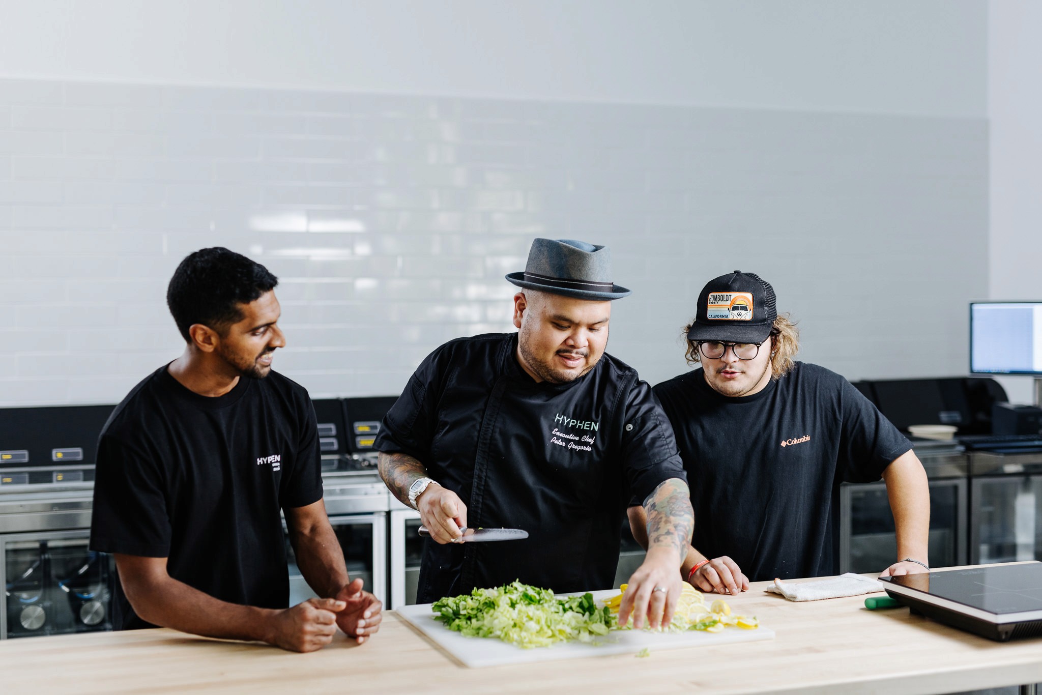Three men standing over a cutting board preparing food