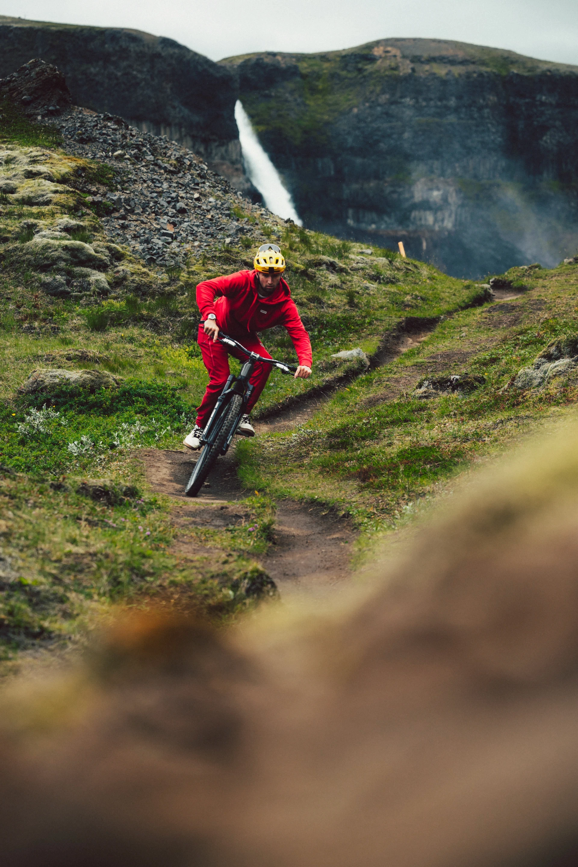 MTB rider in red biking in canyon with waterfall in backround