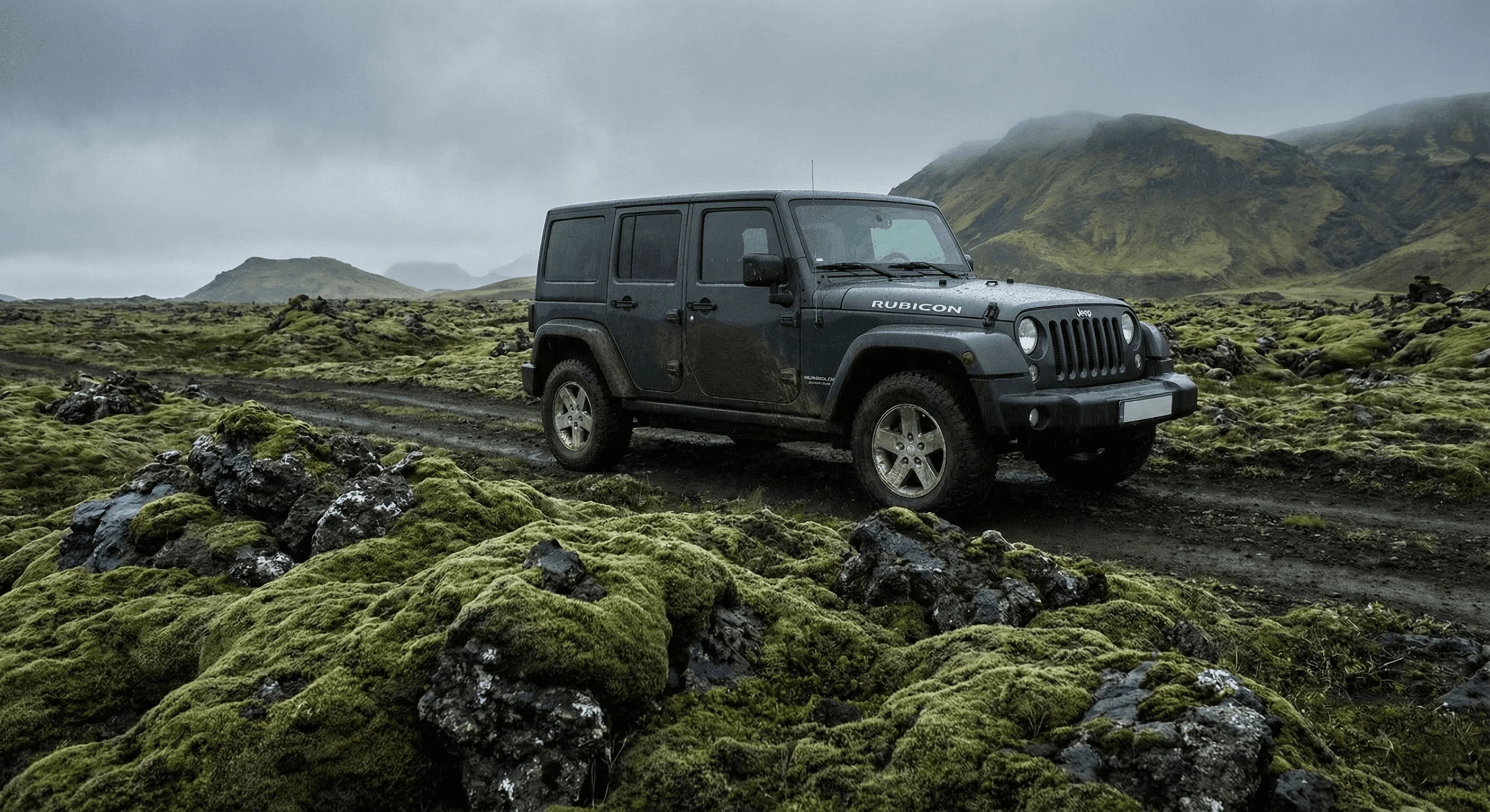 A grey Jeep Wrangler driving on a rough dirt track through a vibrant green, moss-covered lava field.