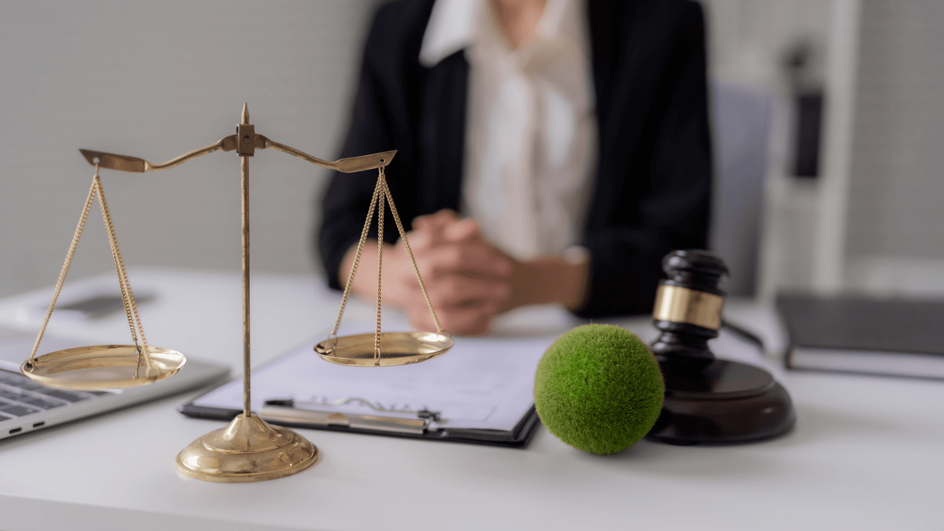 Ein Anwalt sitzt an einem Schreibtisch mit einer Waage der Gerechtigkeit, einem Richterhammer und Dokumenten, was juristische Professionalität symbolisiert.