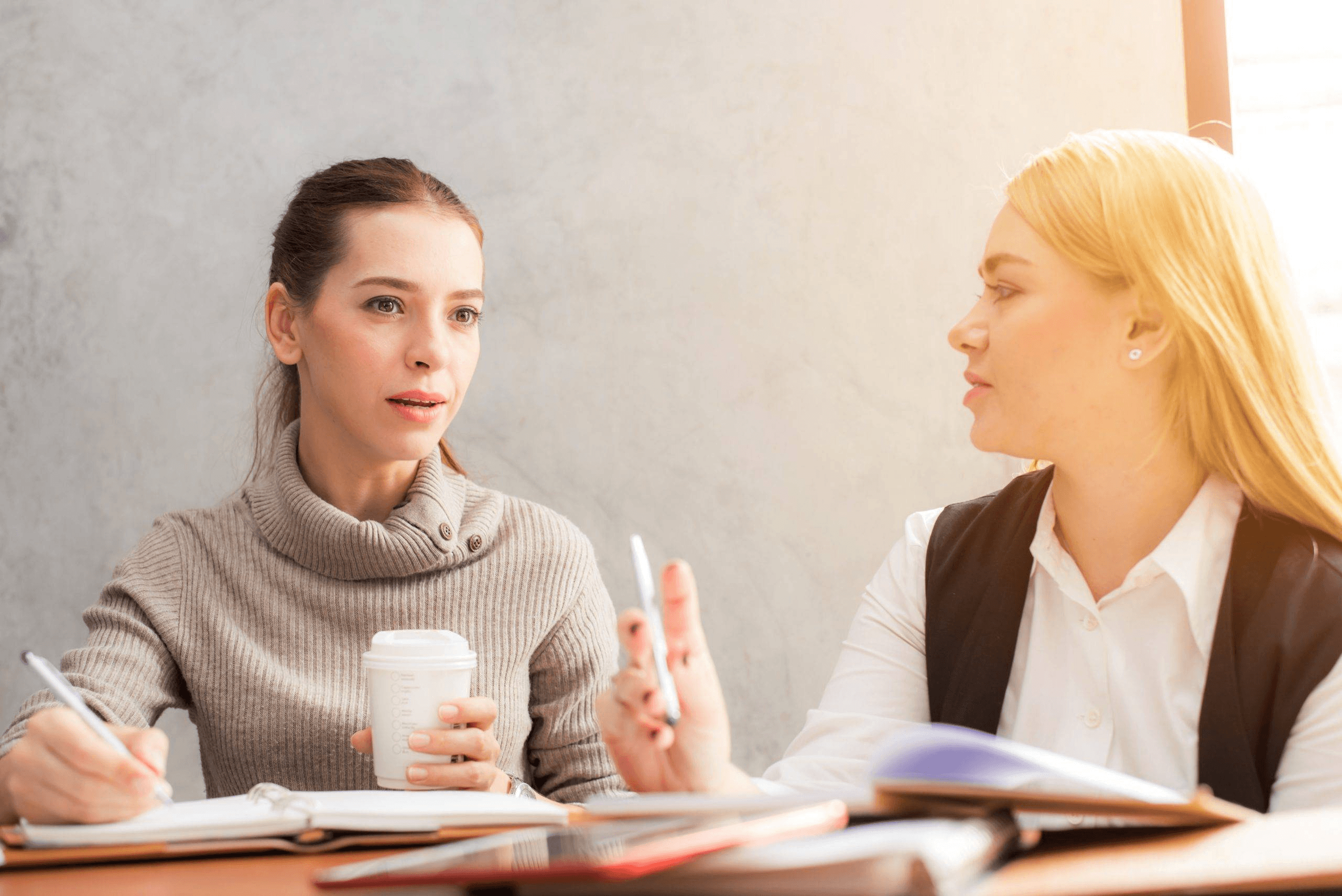 Two women conversing at work desk - best alumni networks colleges