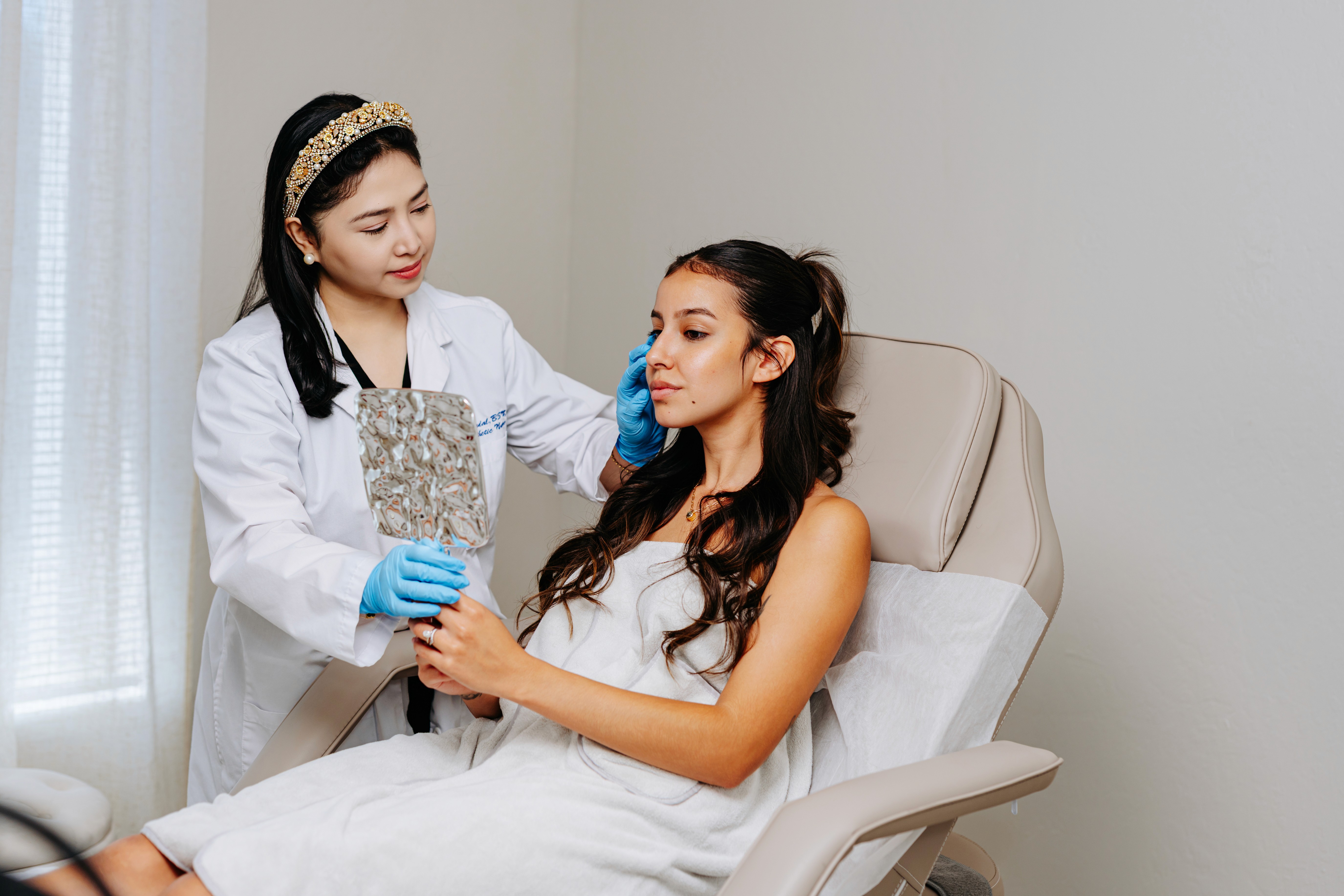 A skin professional assists a patient seated in a treatment chair in a clean, modern clinic setting.