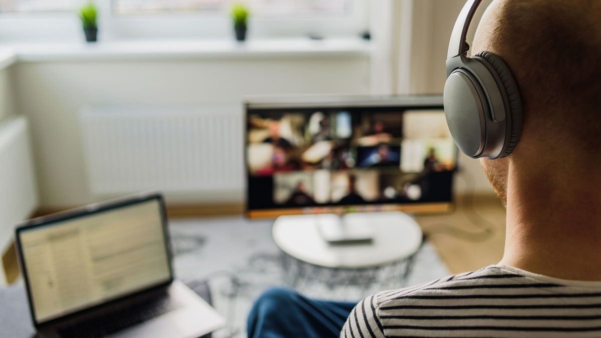 A man taking part in an hybrid workshop while sitting on a sofa a front of two computer screens. 