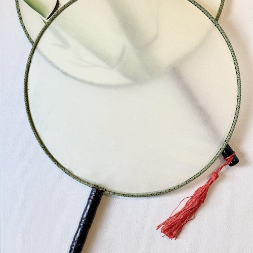 两把传统的圆形手扇，采用浅色织物制作，边缘是绿色的，手柄是黑色的。其中一把挂着一个红色的流苏。