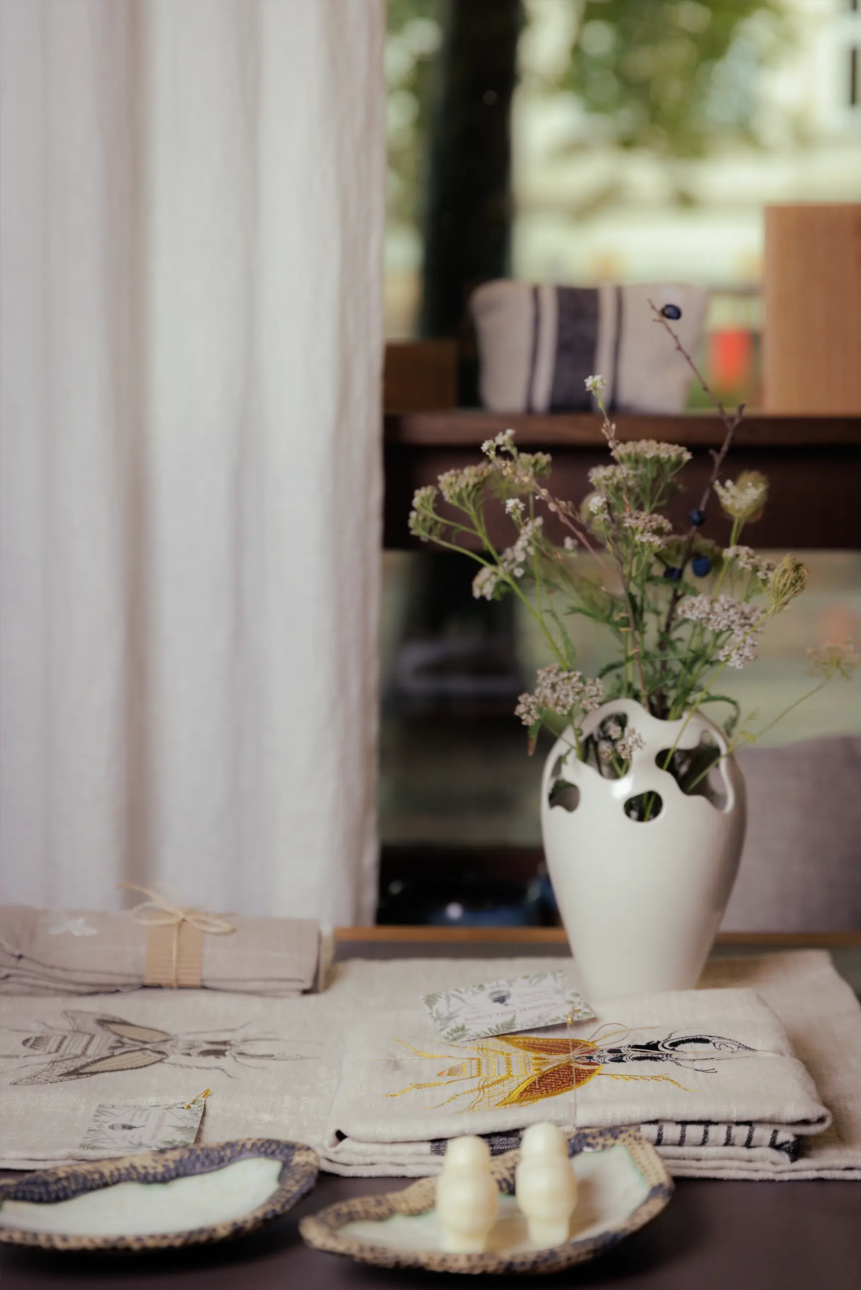 Ein schlichter Tisch mit handgestickten Leinenkissen, Servietten und einer Vase mit Wiesenblumen