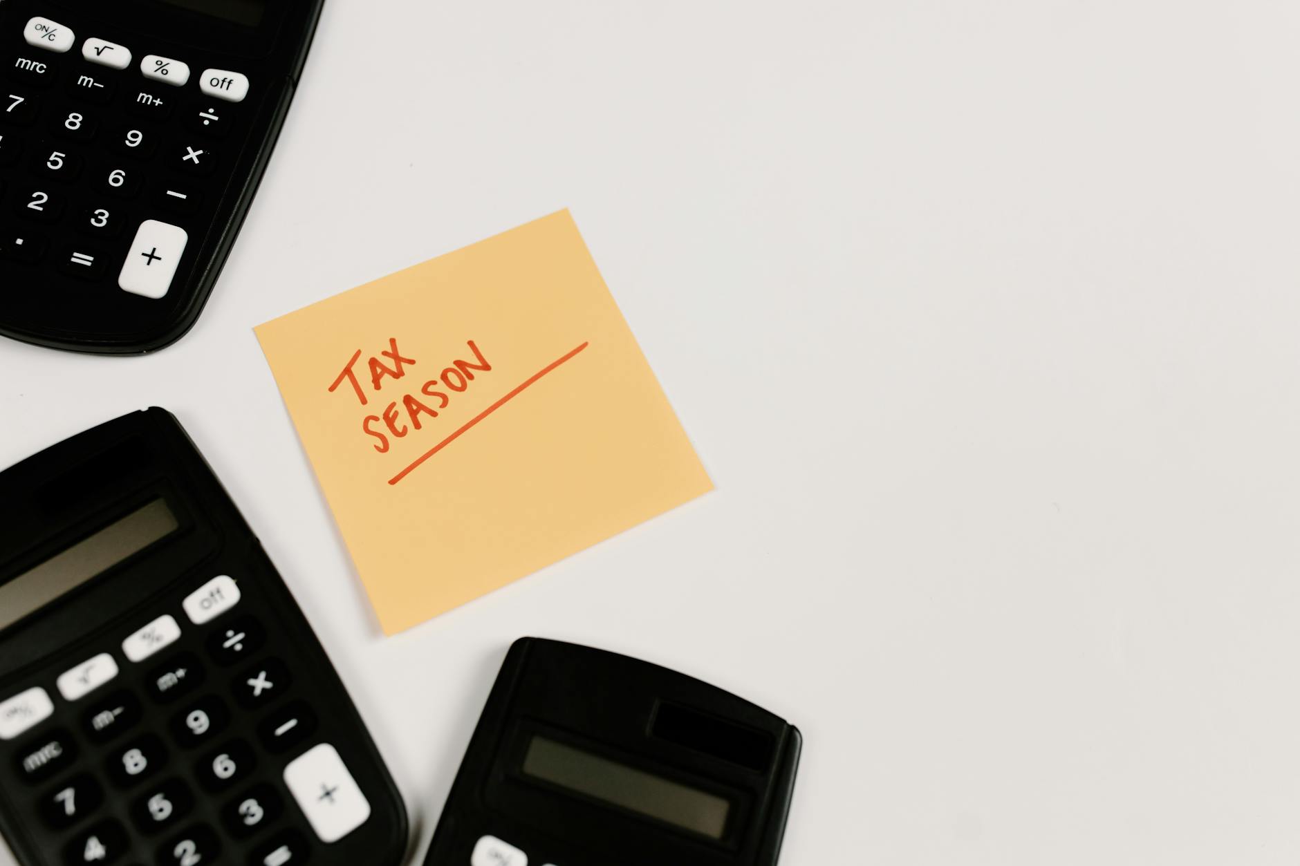 Three calculators arranged around a sticky note reading Tax Season in red writing on a white background