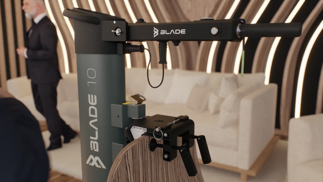 Close-up of the Blade 10 electric outboard motor's control arm and mounting clamp displayed in a showroom, with a man in a suit walking past a white sofa in the background.
