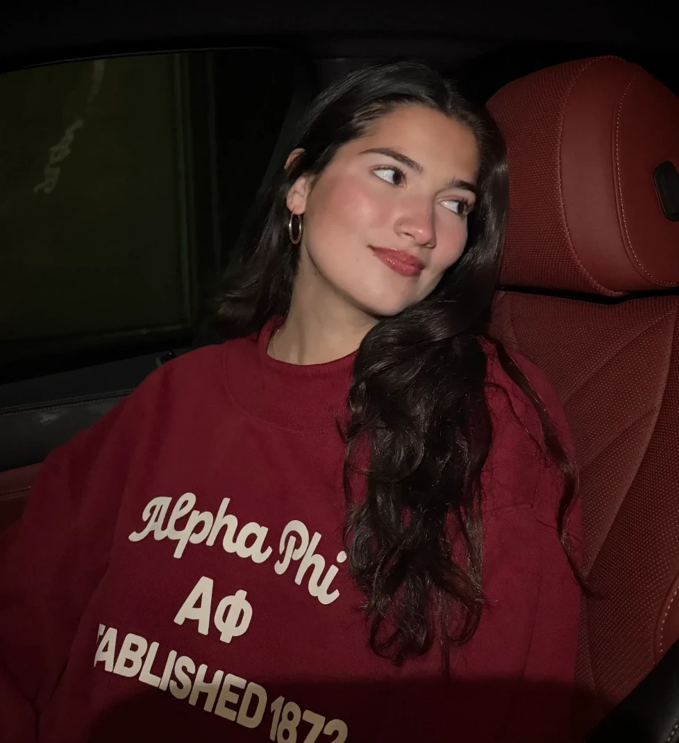 Person sitting in a car wearing a red “Alpha Phi” sweatshirt