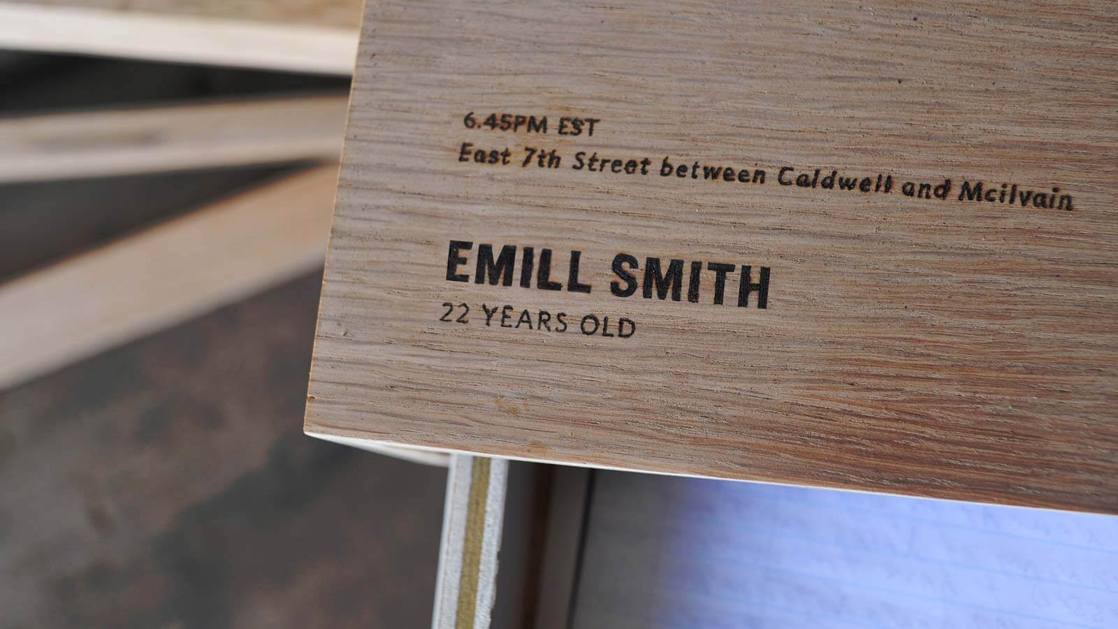 Wooden plaque with engraved text showing time, location and age information for an art exhibition or memorial display