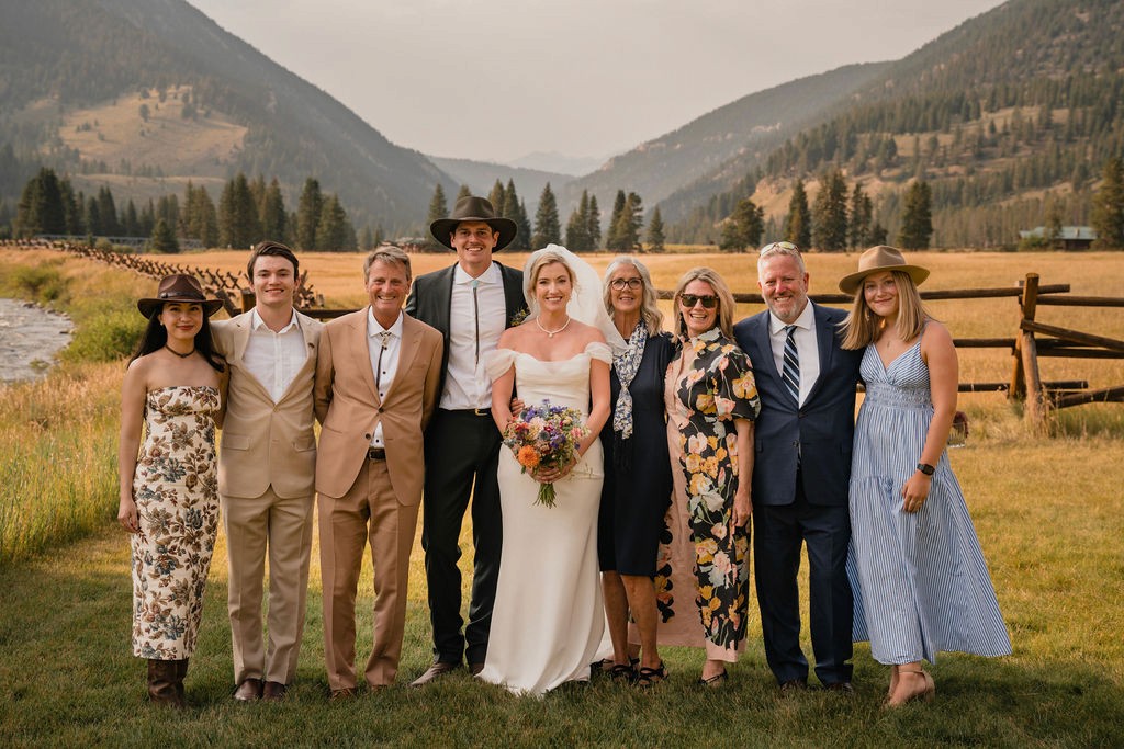 Newlyweds posing with family members in a mountain valley