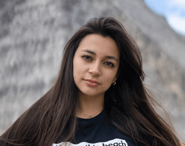a young man wearing glasses standing in front of a mountain