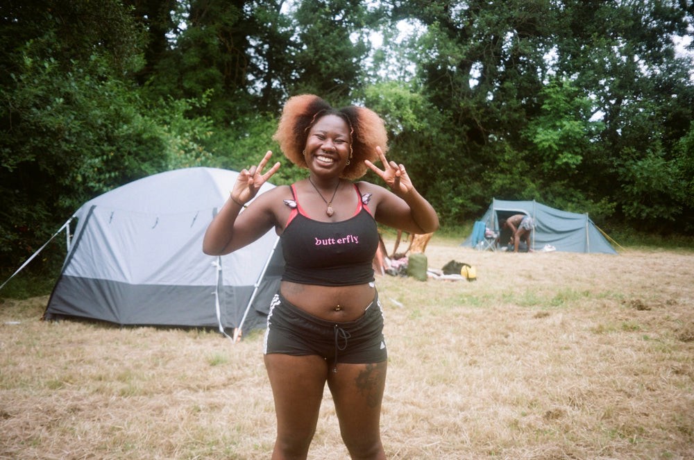 A person smiles while giving peace signs in front of a tent
