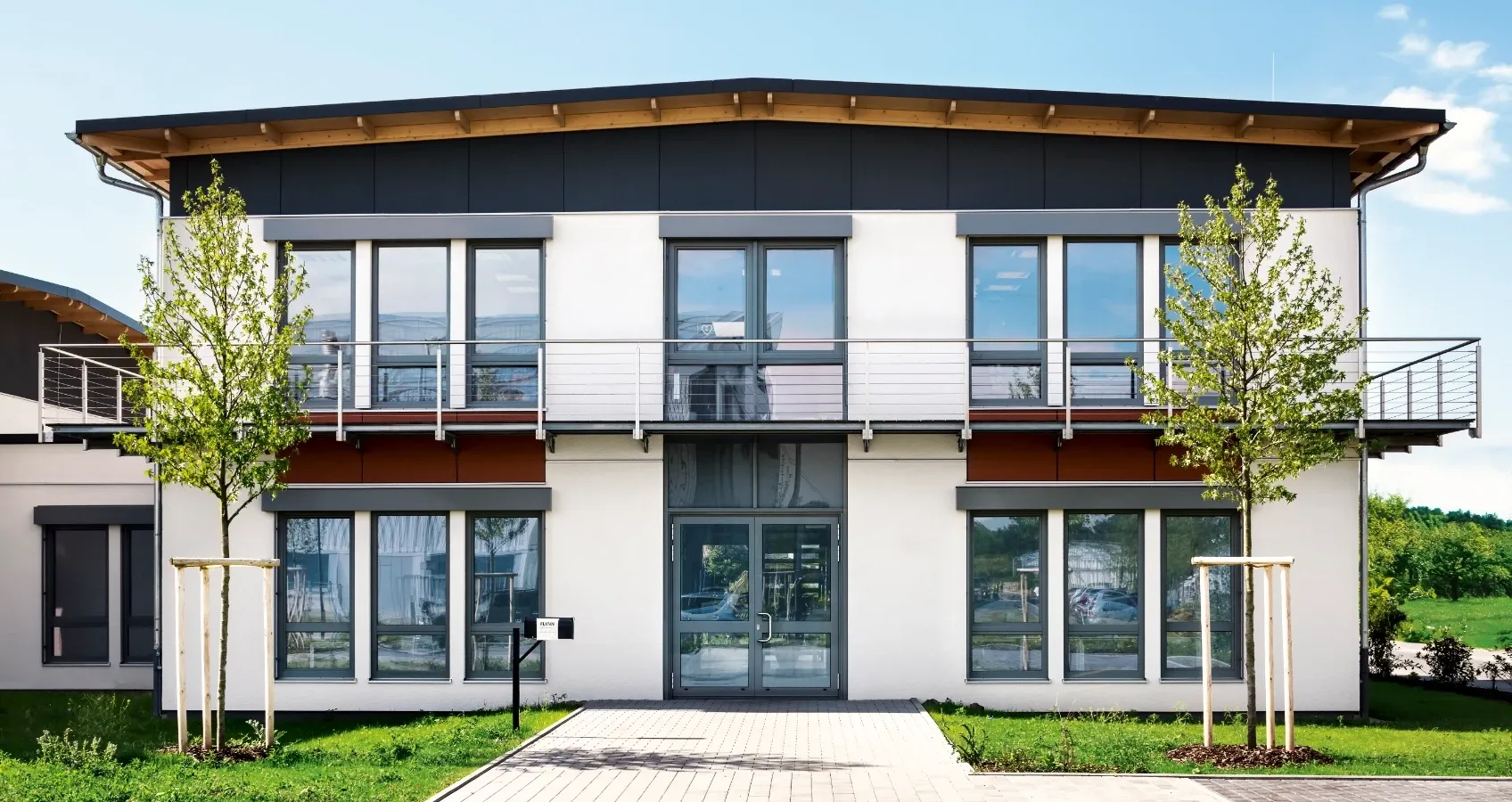 Modernes Bürogebäude mit Glasfront, Balkonen und umliegendem Grün.