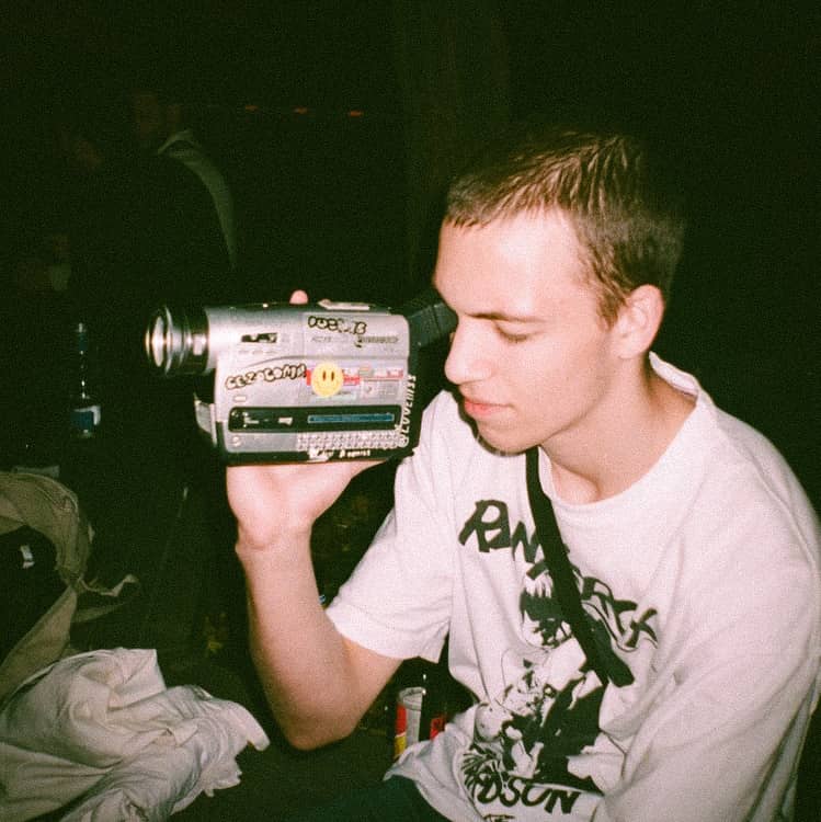 Junger Filmemacher hält eine Vintage-Videokamera mit Aufklebern, analoge Filmwurzeln, BLINKHAUS Filmstudio