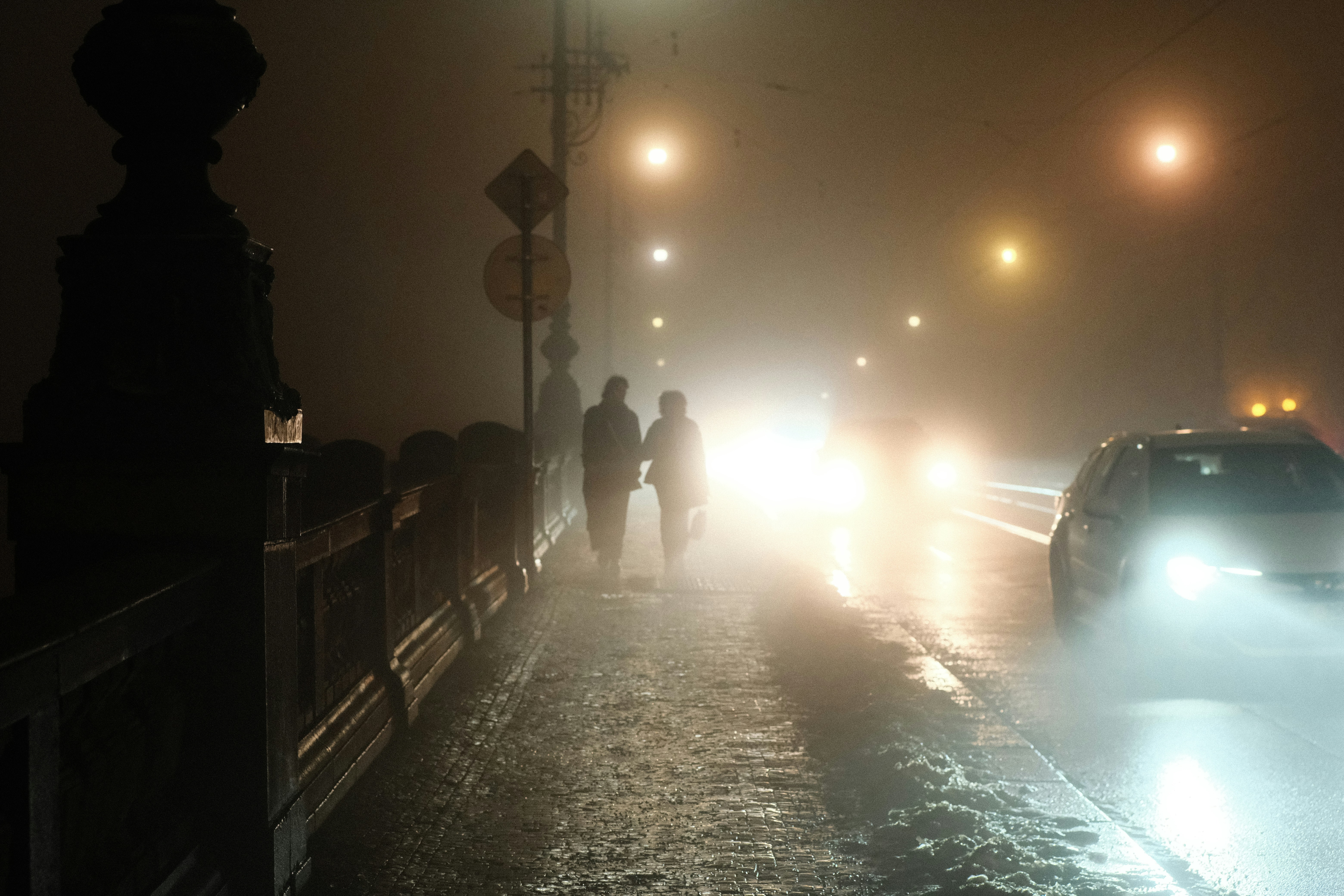 Two people walk on a foggy street at night.