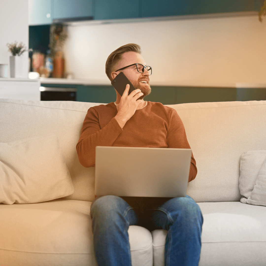 een man die op de bank achter zijn laptop aan het bellen is