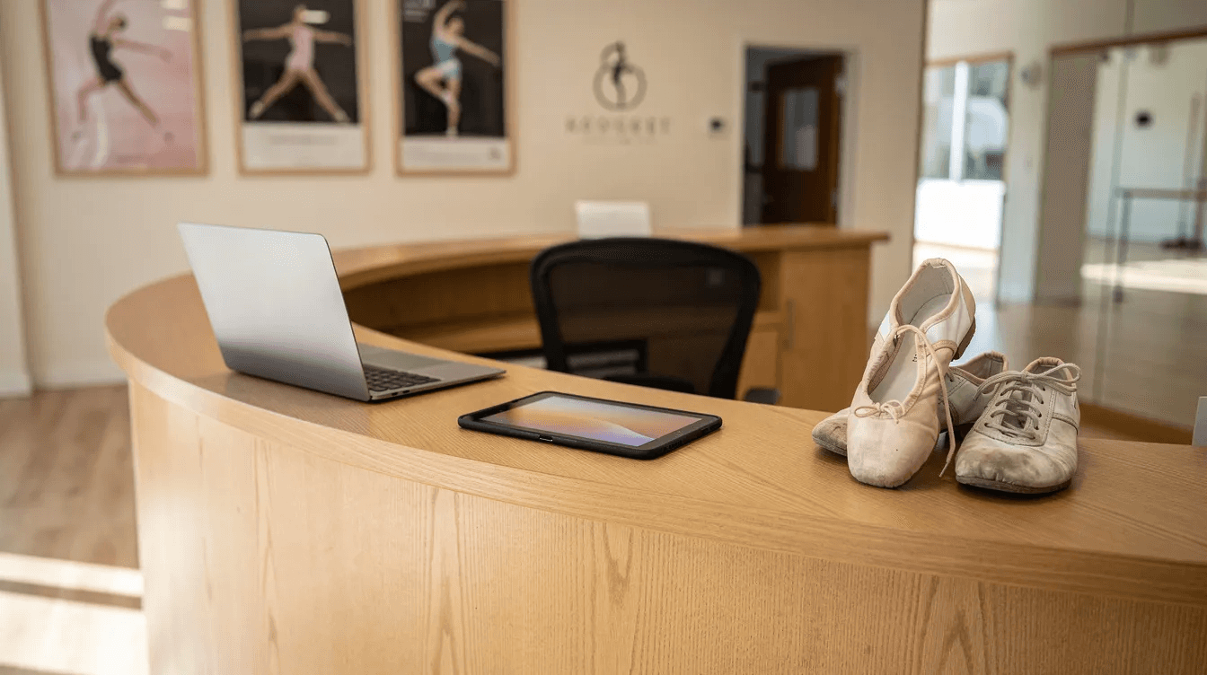 The image depicts a welcoming studio reception desk featuring a laptop and tablet, with a pair of dance shoes placed nearby, suggesting a vibrant environment for managing class registrations and attendance tracking for students in various programs. This setup highlights the importance of organization and efficient management software for sports clubs and dance schools.