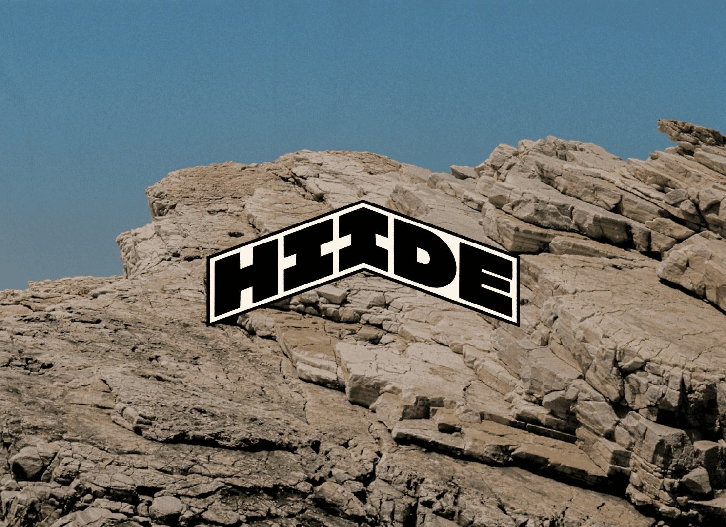 Logomark spelling "HIIDE" on a rocky landscape with a clear blue sky in the background.