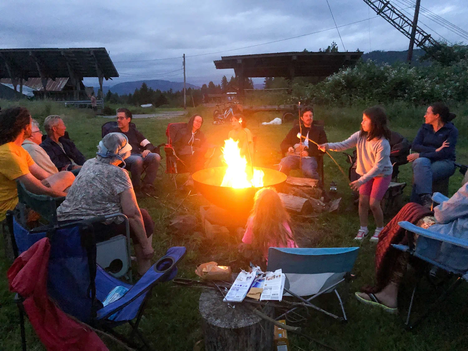 Community members gathered outdoors around a shared fire pit during an evening gathering.