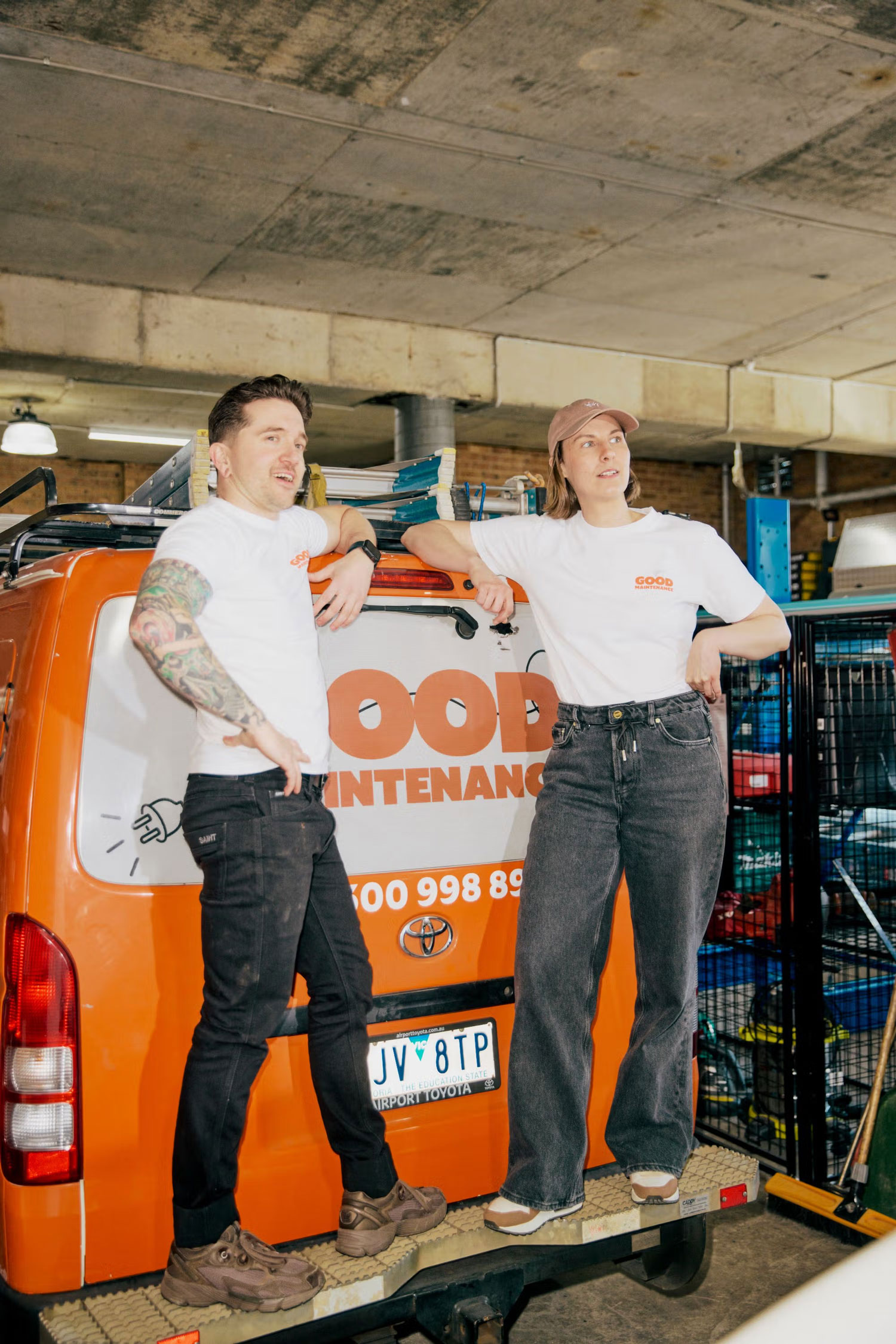 Two Good Maintenance team members leaning against a branded service van inside the workshop.