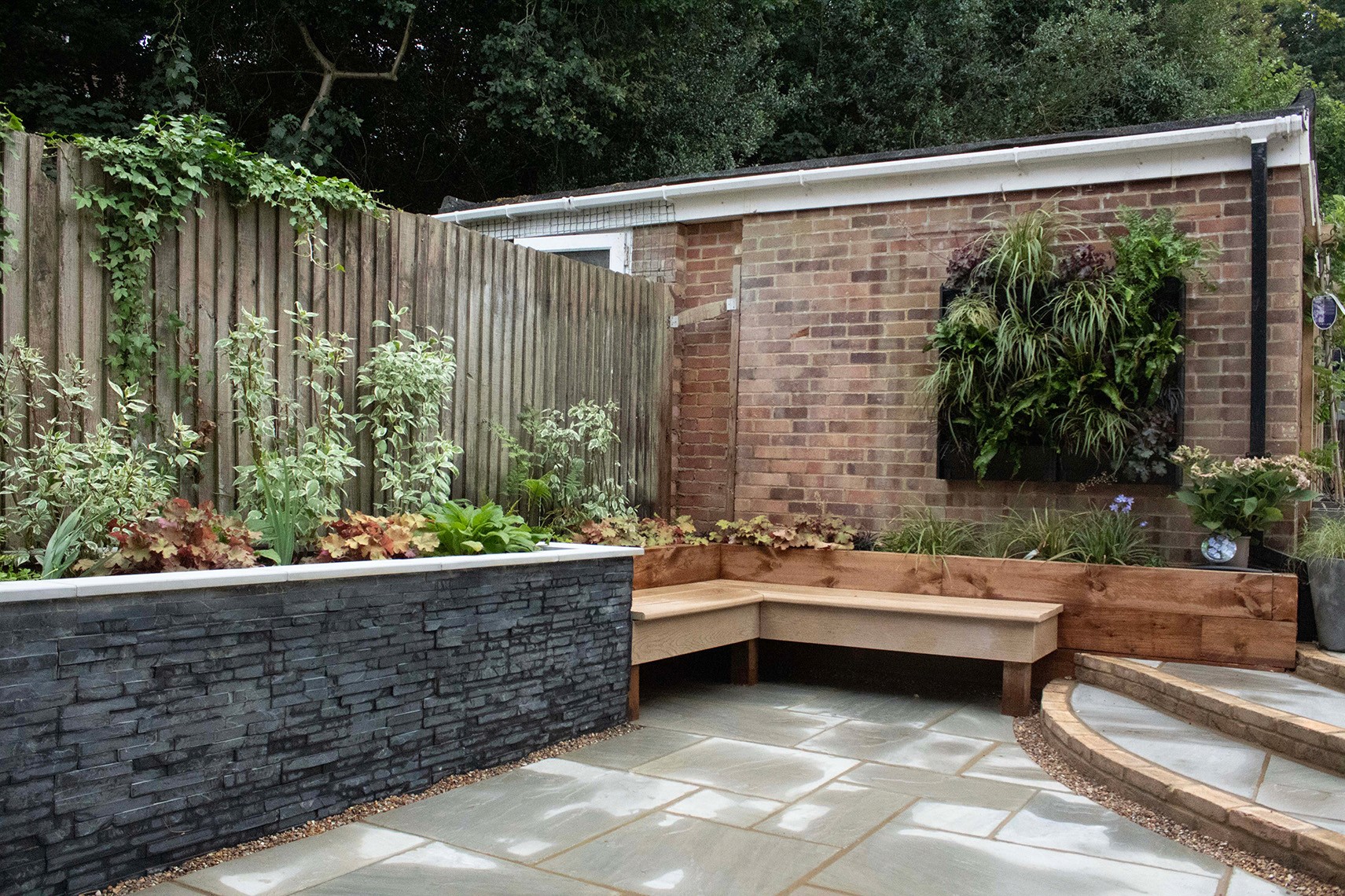A landscaped garden area with stone walls, wooden seating, and various plants in a serene setting.