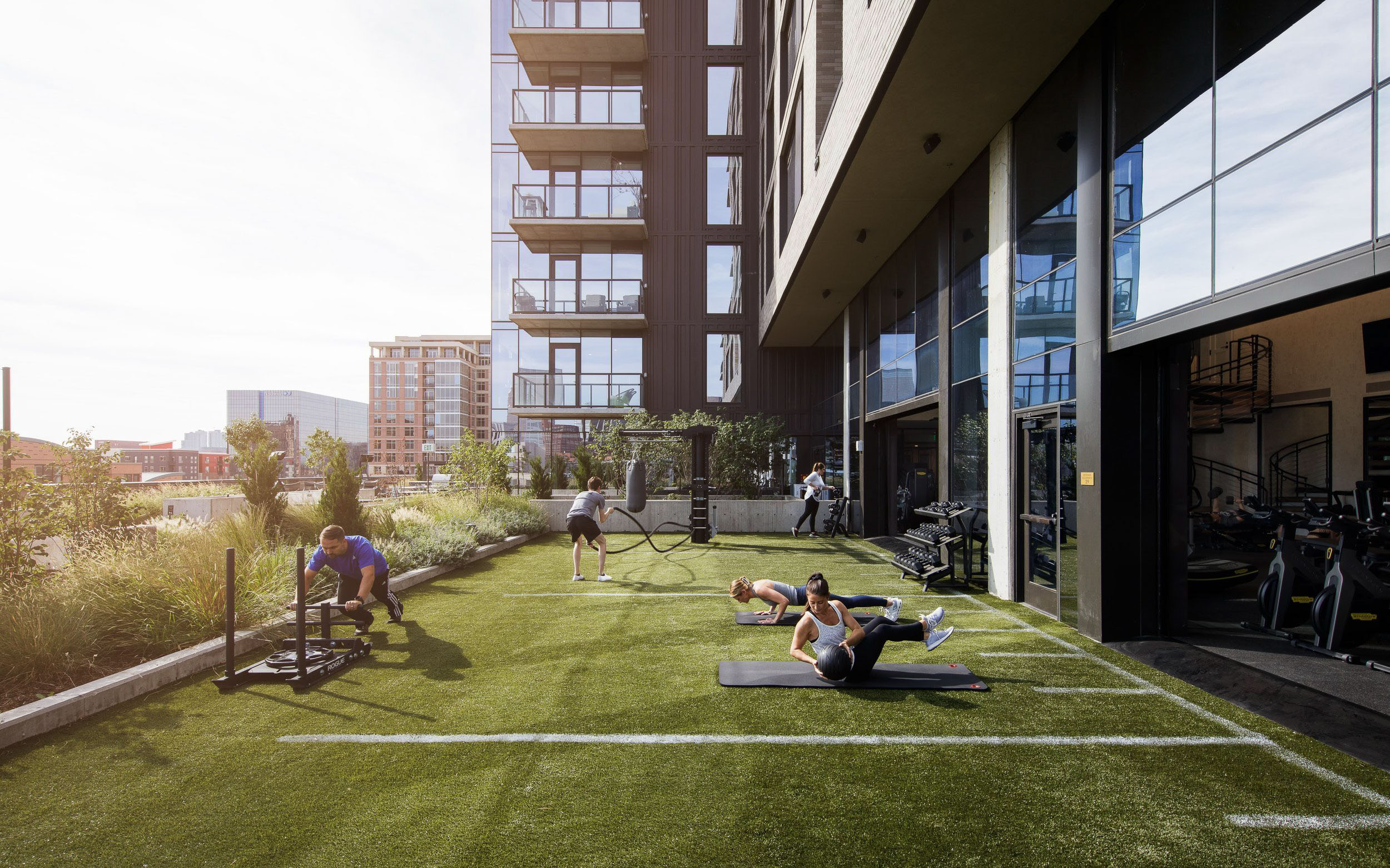 People exercising on an outdoor gym turf area beside a building.