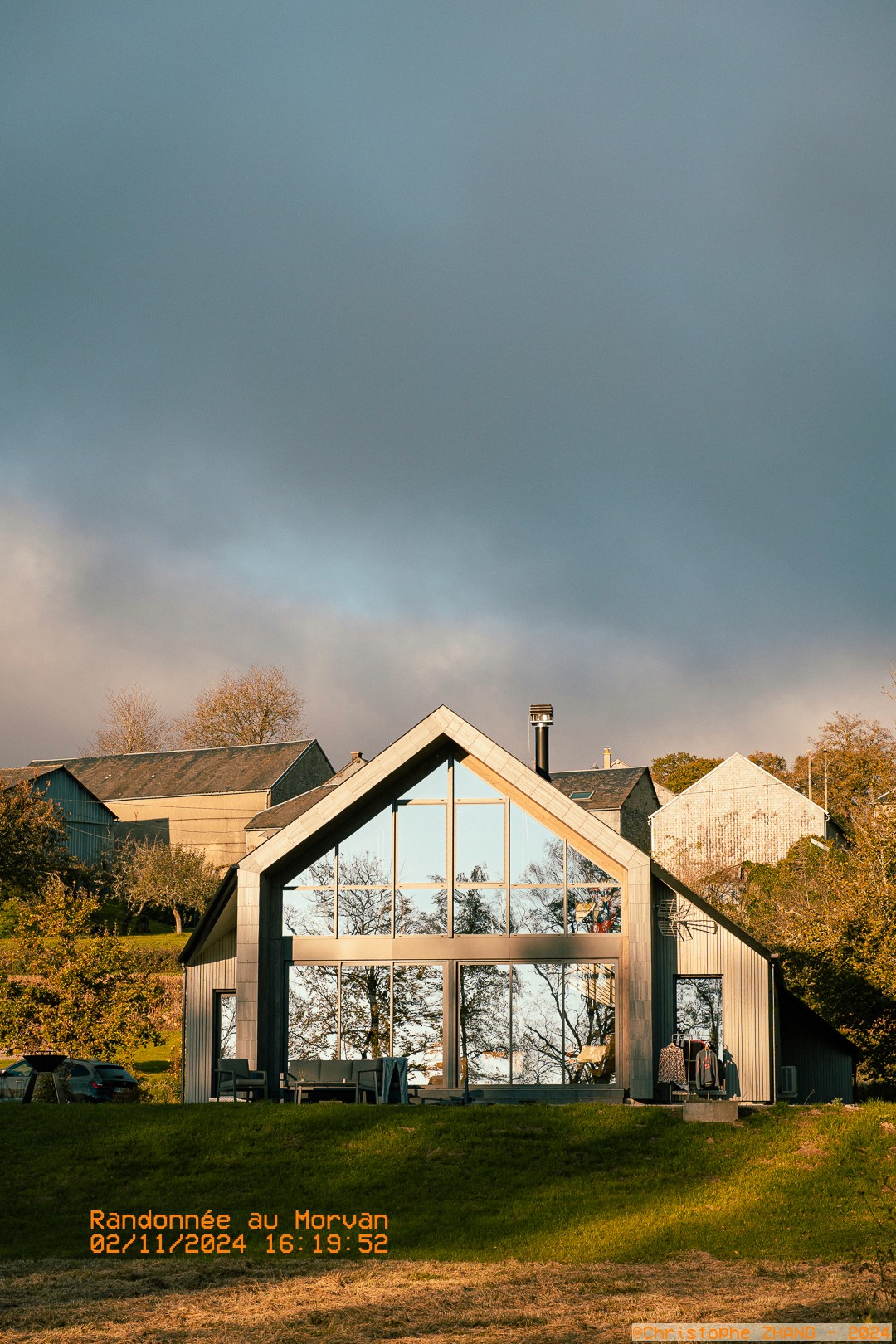 Architecture contemporaine au cœur de la campagne, avec des bâtiments traditionnels en arrière-plan.
