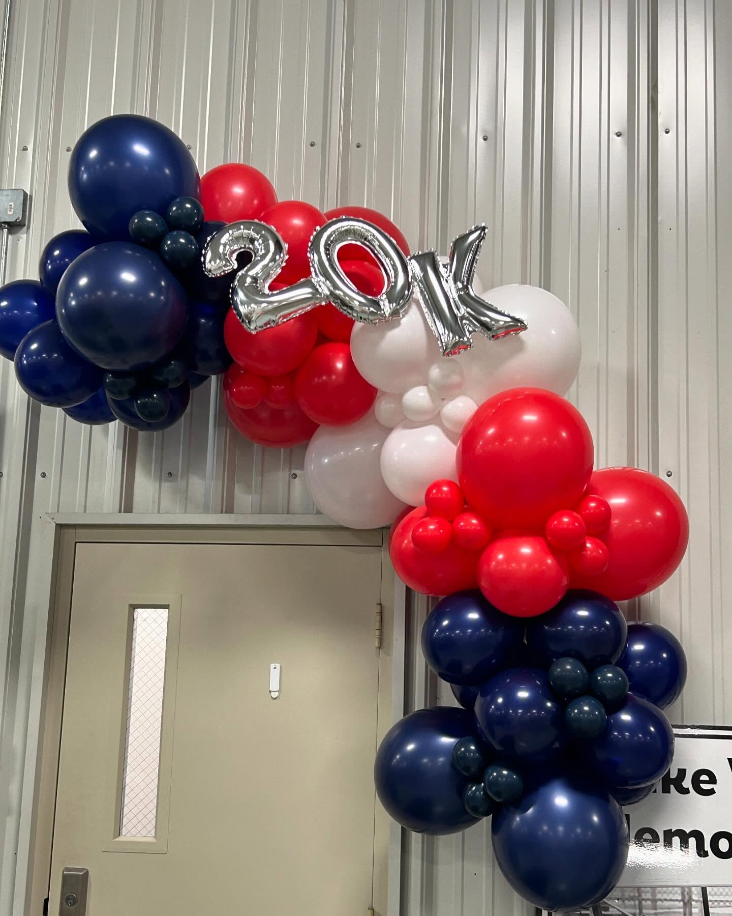 Red, white, and blue balloon garland with metallic accents displayed against white curtains for a patriotic event by Be Bold Balloons