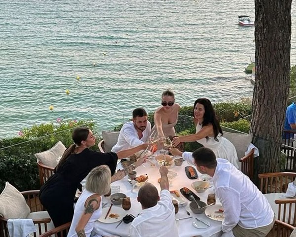 Outdoor lounge under a wooden pergola, draped linen curtains, beige cushions, ocean backdrop, palm shadows dancing on the walls, serene luxury.