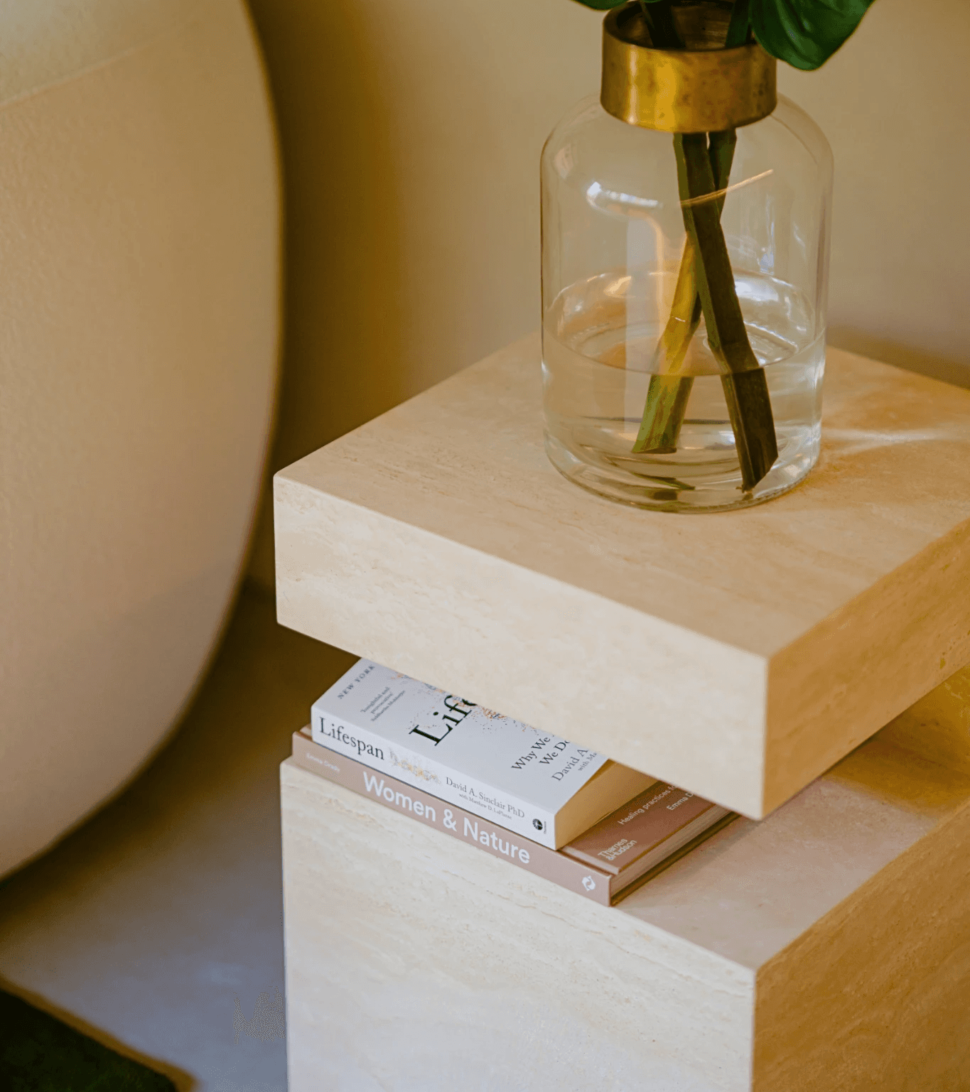 A plant in a transparent vase placed on a small coffee table, with books stacked underneath it.