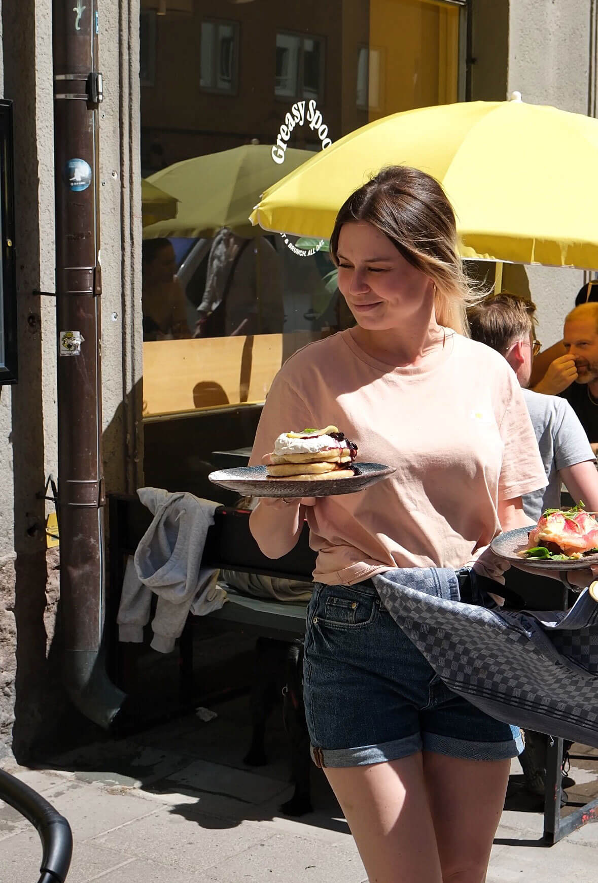 Server walking outside carrying two dishes while smiling.