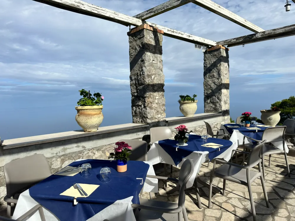 A restaurant terrace in Anacapri with blue-clothed tables under a stone pergola, looking out to sea.