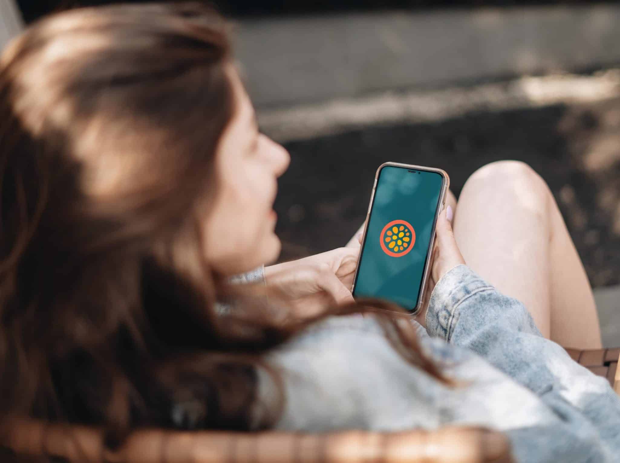 Woman using smartphone with app icon on screen, outdoor setting.