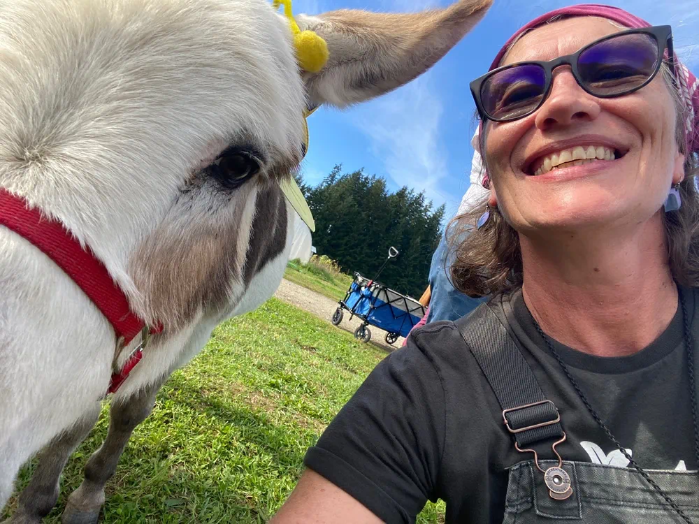 A person smiling beside a donkey at Rooted Northwest.