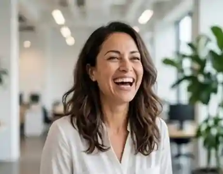 Headshot of a joyful female executive in a white blouse, standing in a bright, modern office environment with plants.
